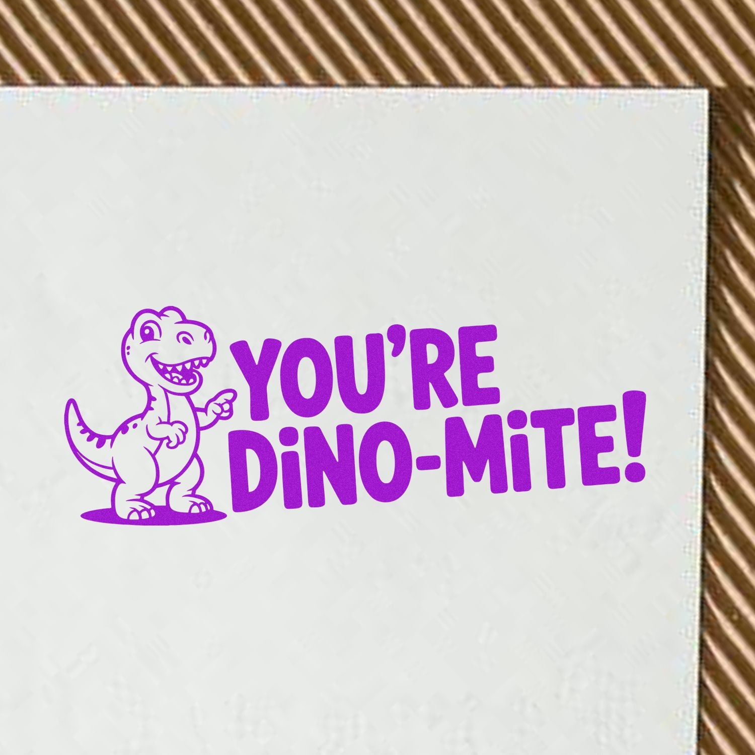 Purple dinosaur rubber stamp seal with YOURE DINO-MITE! text on white paper.