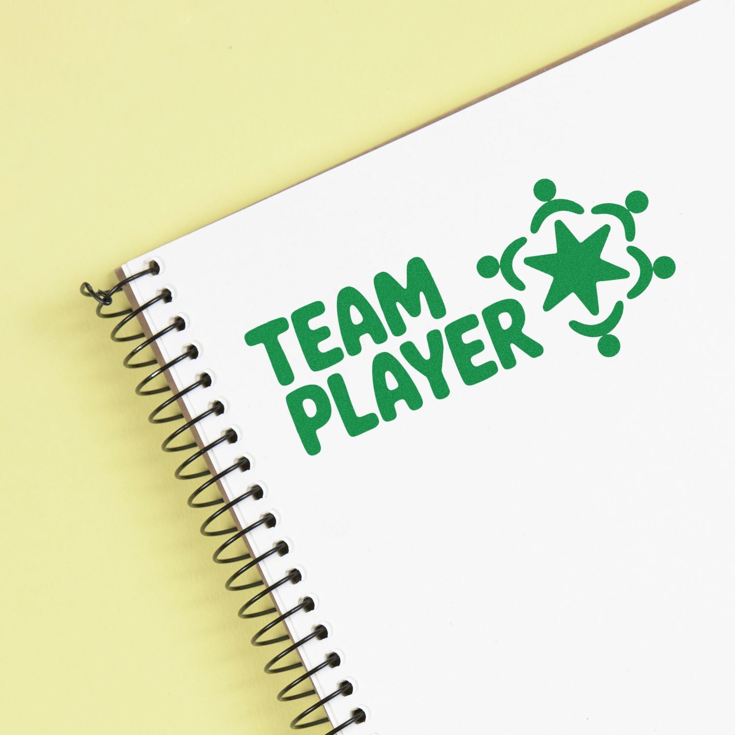 Green TEAM PLAYER stamp and seal on a white spiral notebook with a pale yellow background