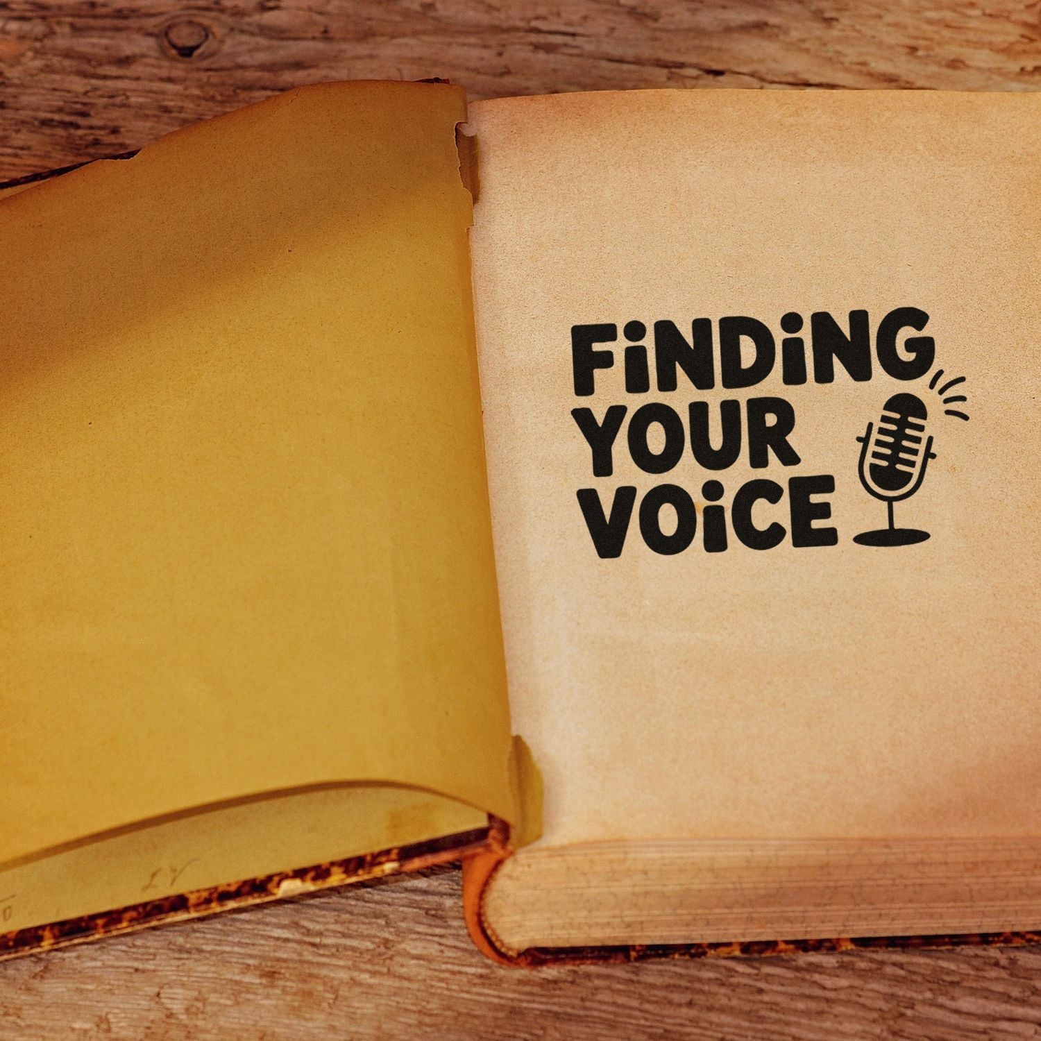 Open vintage book with black Finding Your Voice rubber stamp seal and microphone on tan pages over wood.