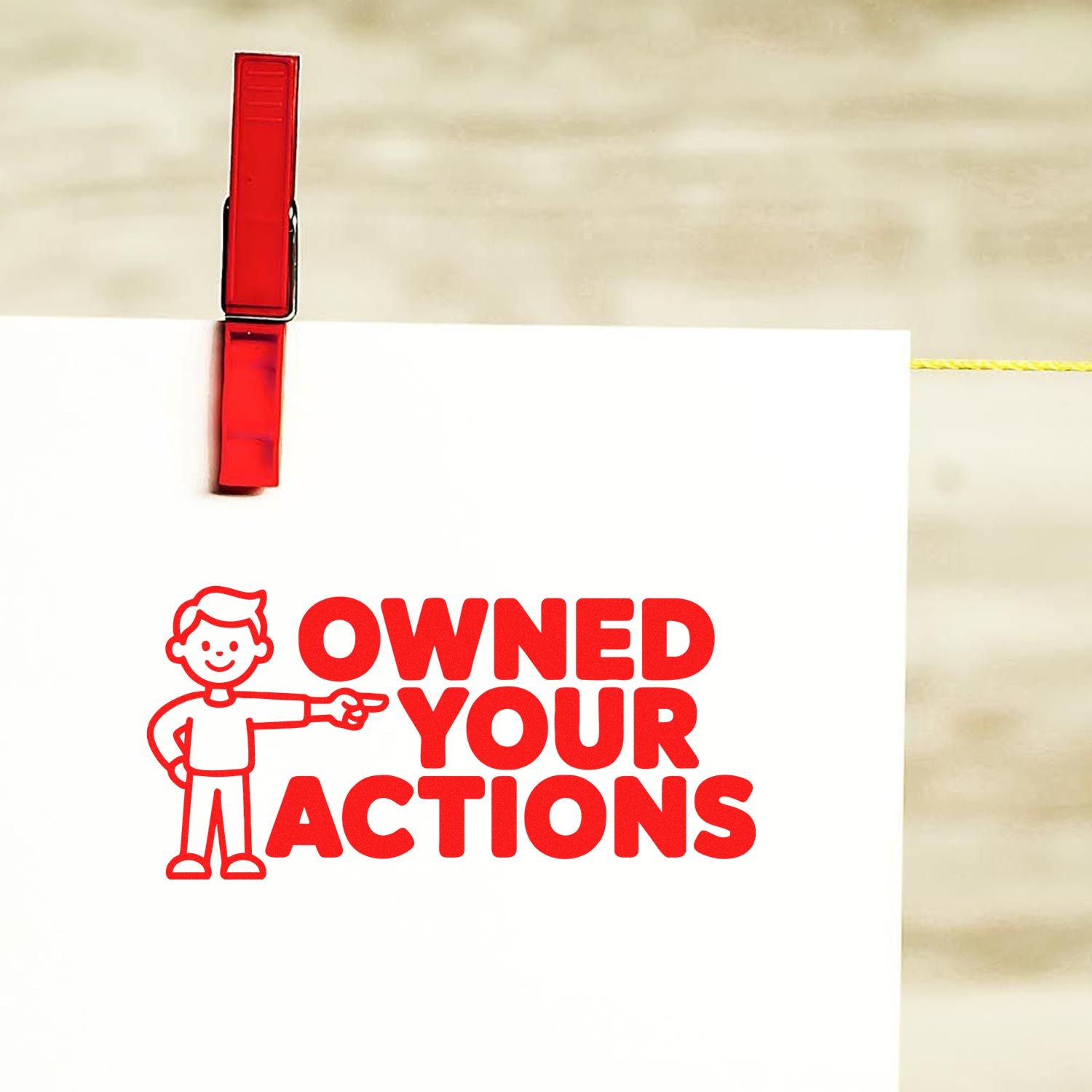 Red self-inking stamp seal on white card reading OWNED YOUR ACTIONS with a pointing cartoon figure.