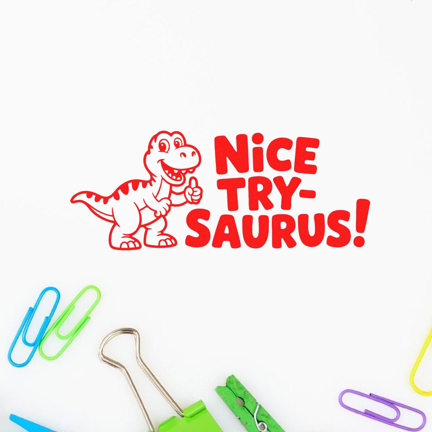 Red dinosaur stamp seal reading "Nice Try-saurus!" with colorful paper clips on a white background.