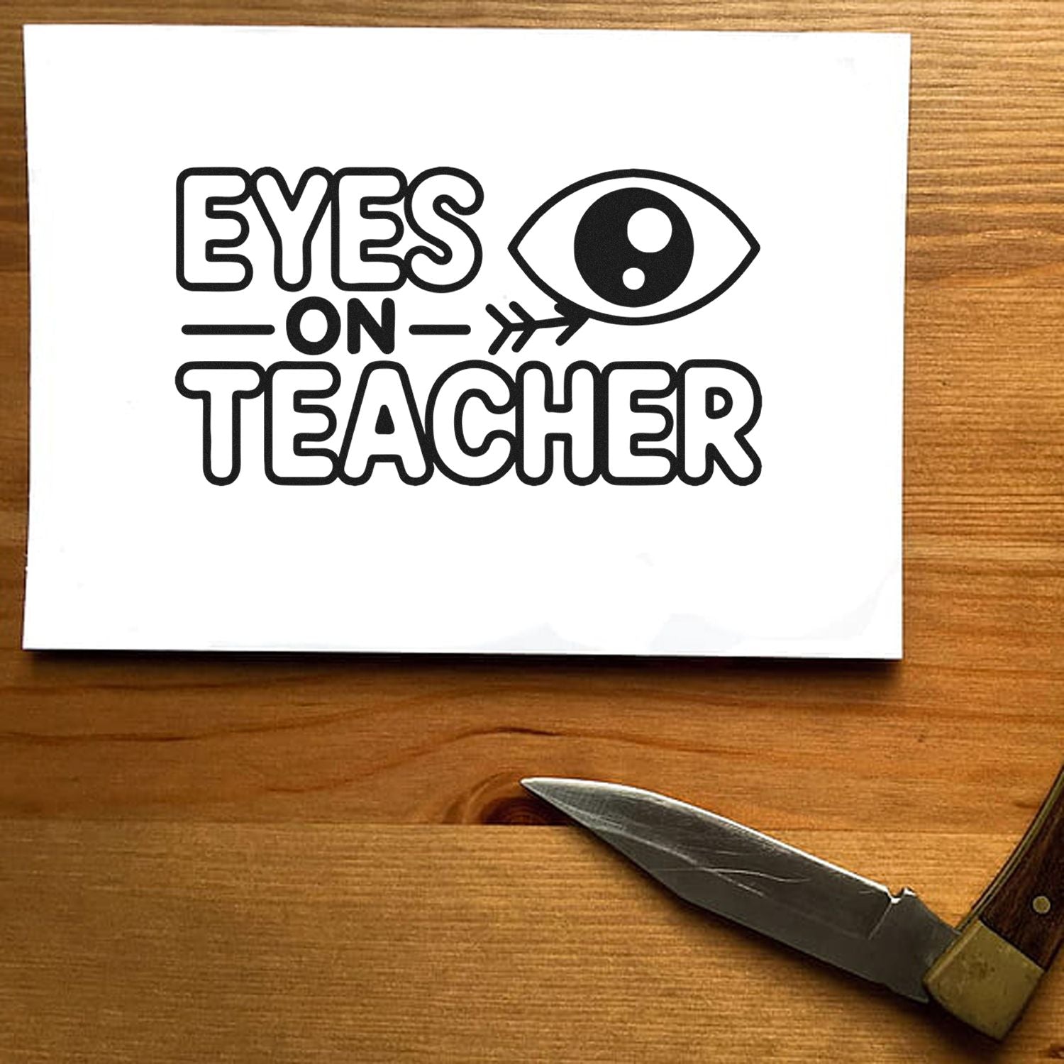 Black Eyes on Teacher stamp/seal design with eye icon on white paper, on a wooden tabletop.