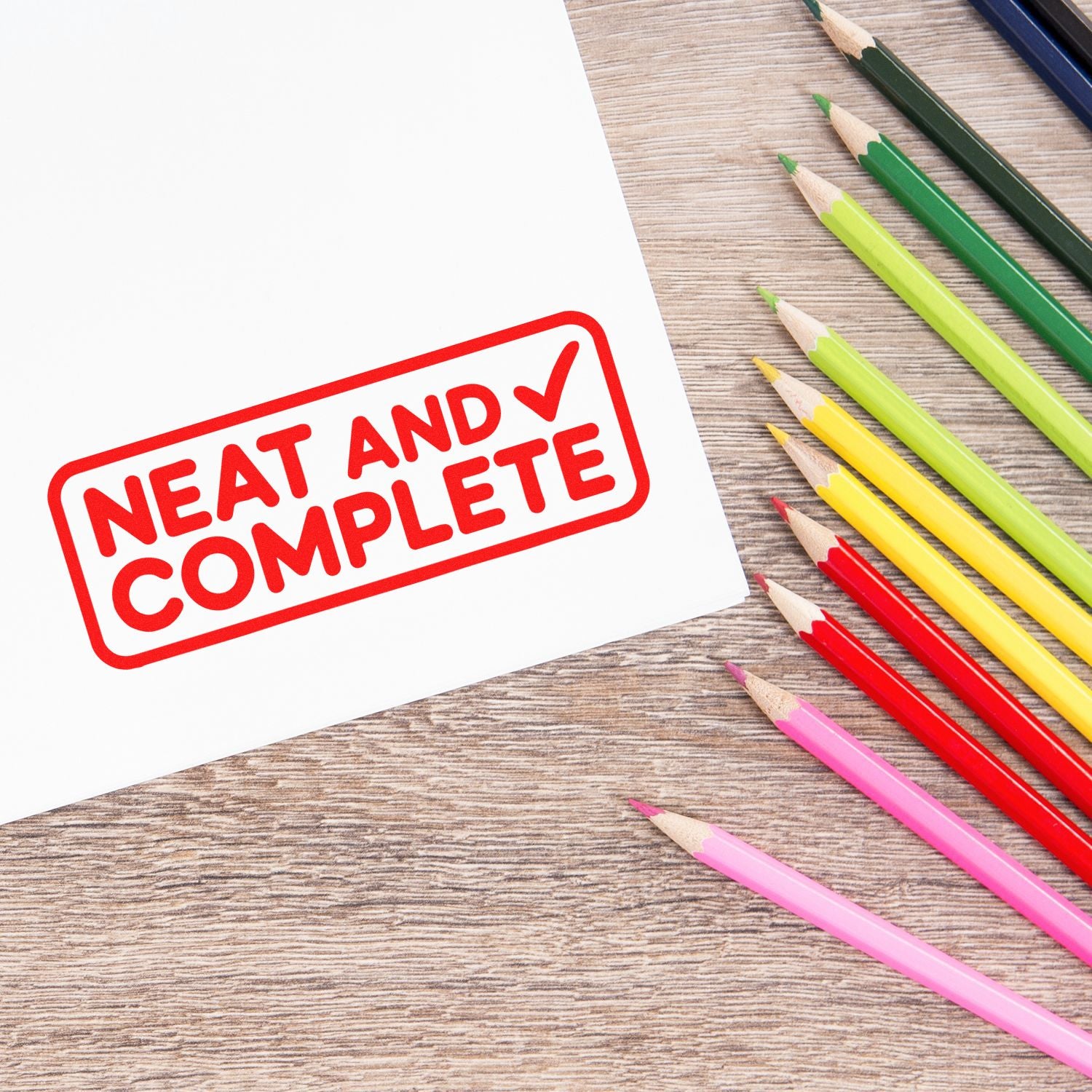 Red Neat and Complete stamp seal on white paper beside colorful pencils on a wood desk