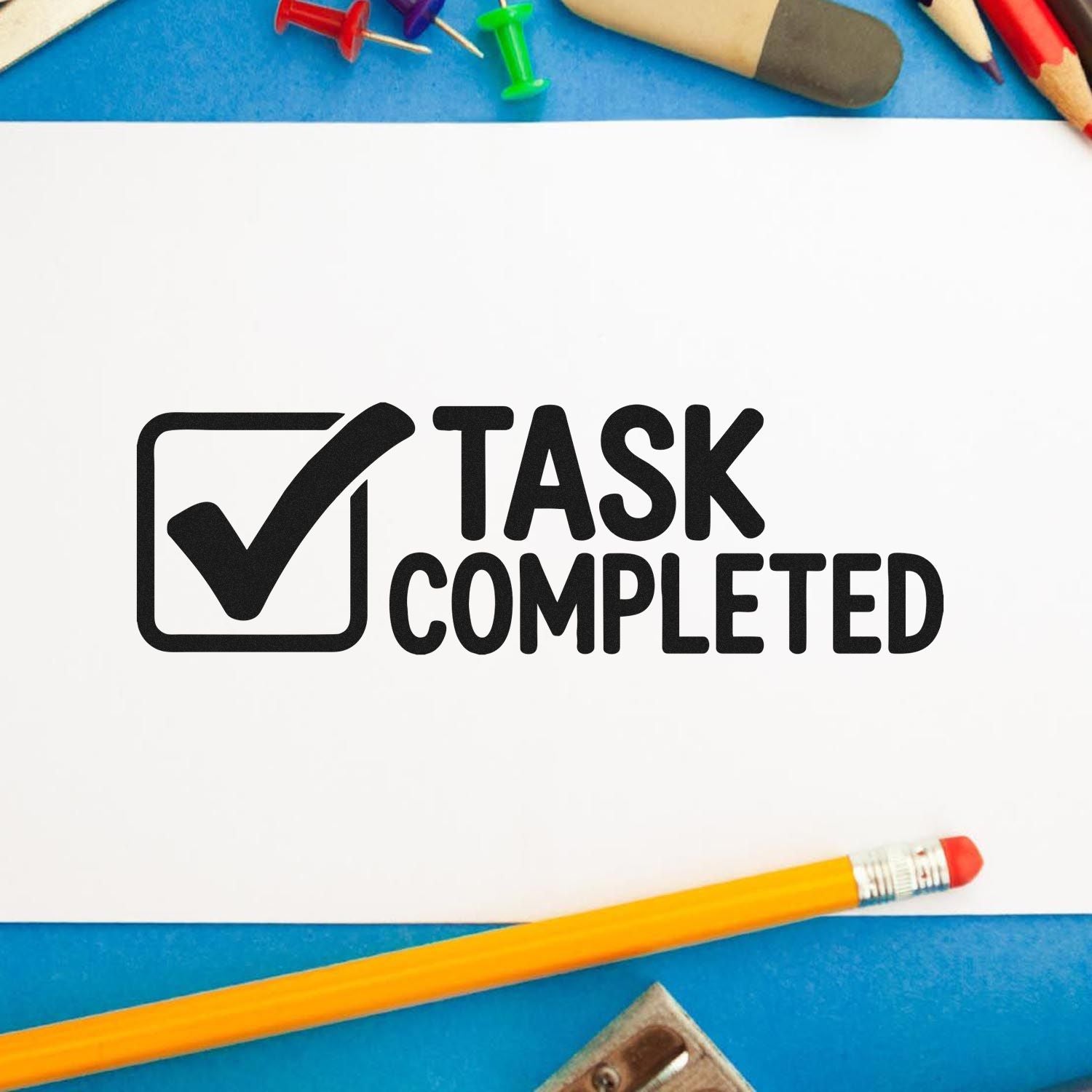 Black task completed stamp seal with checkmark on white paper, surrounded by colorful pencils on a blue background.
