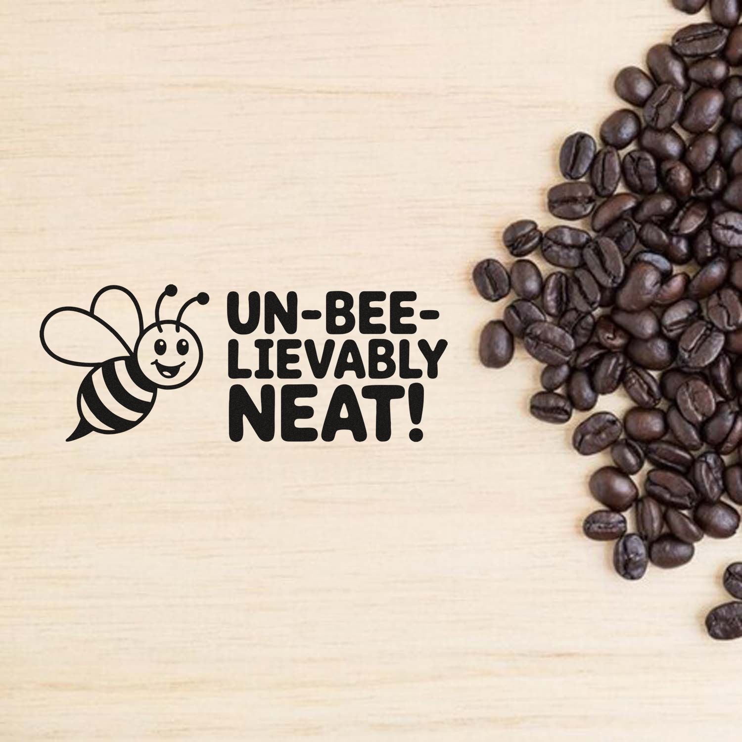 Black bee stamp seal with UN-BEE-LIEVABLY NEAT! beside dark coffee beans on light wood.