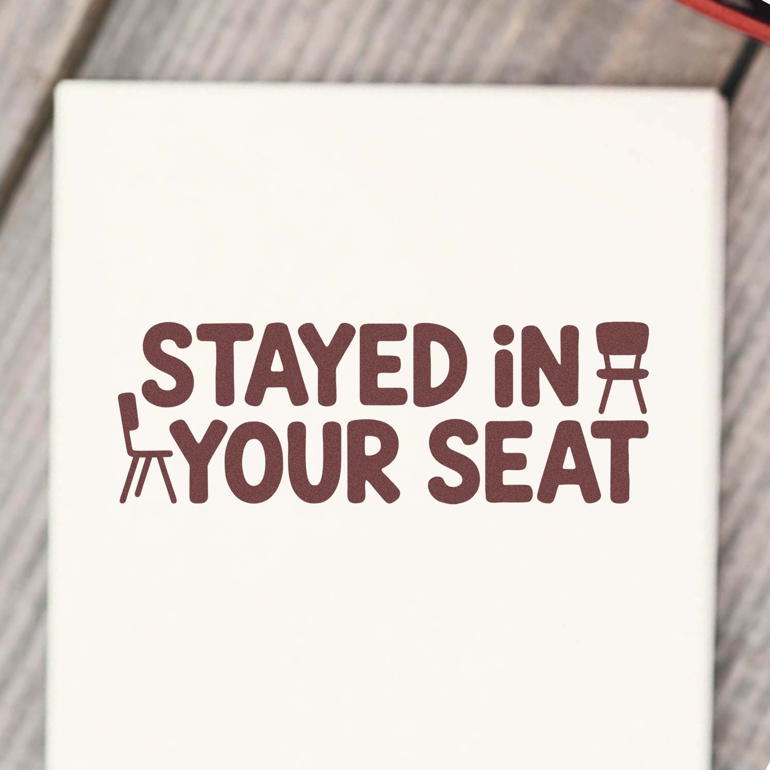 Maroon STAYED IN YOUR SEAT stamp seal design with chair icons on a cream background.
