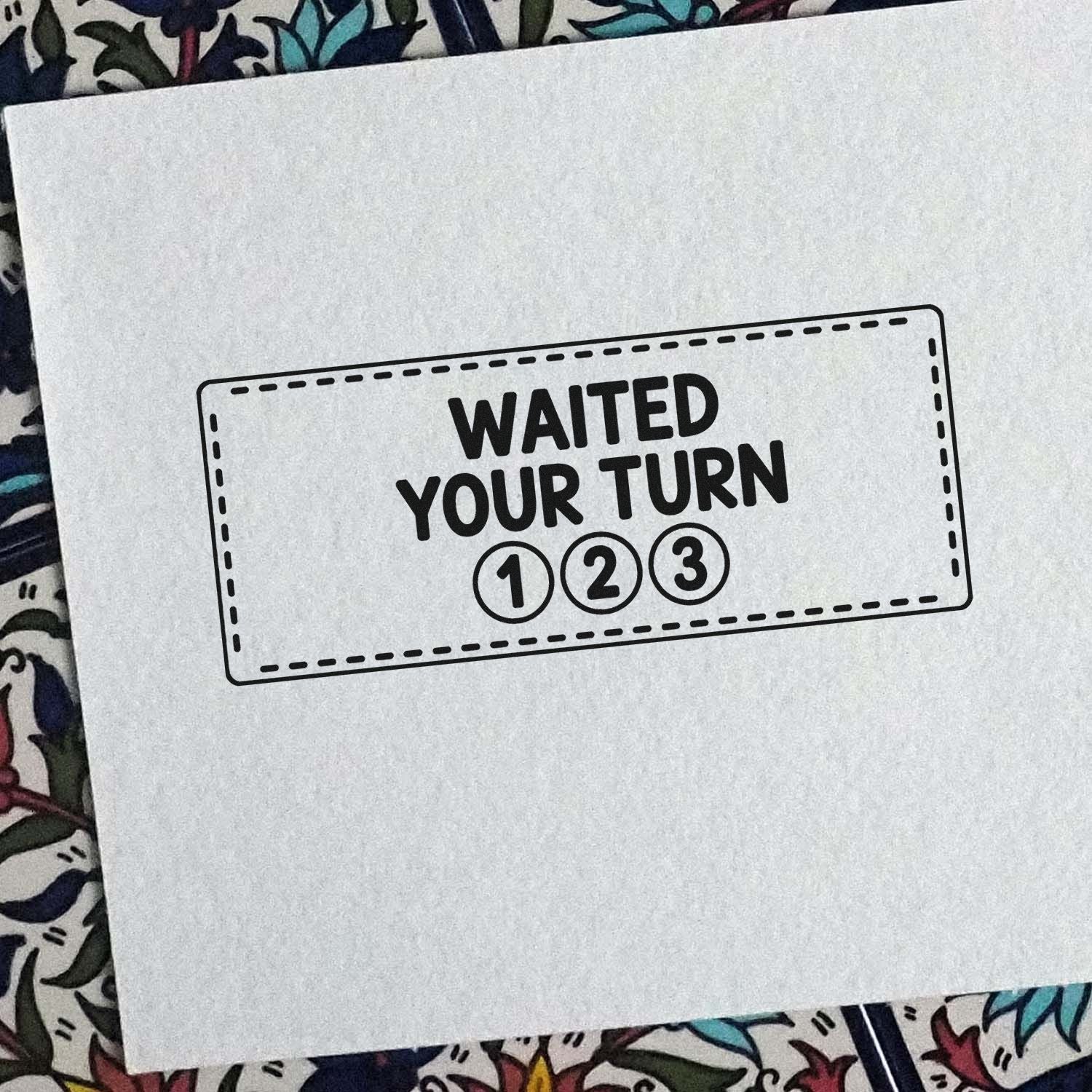 Black WAITED YOUR TURN stamp and seal design with 1, 2, 3 in circles on white paper over colorful patterned fabric.