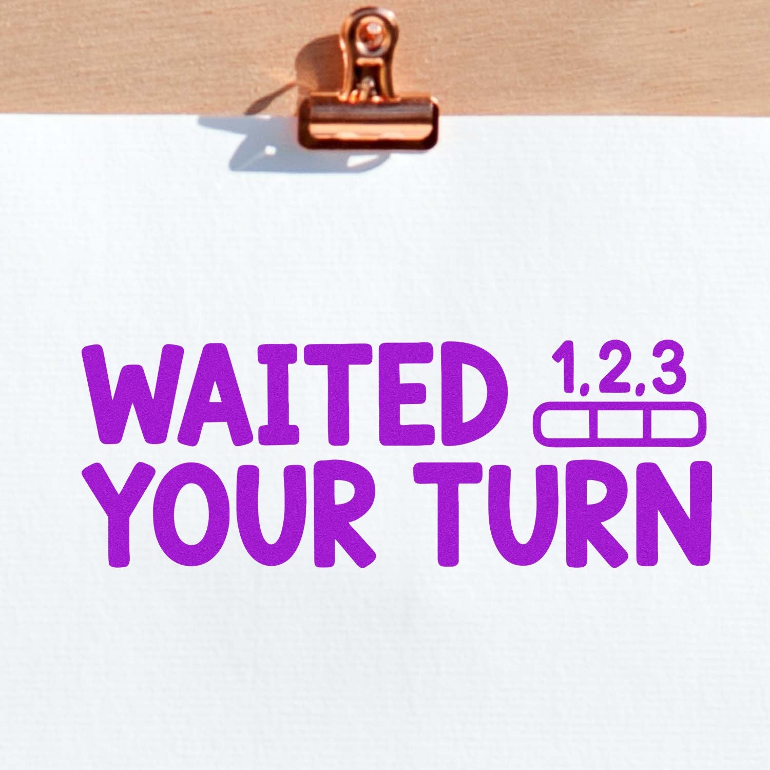 Copper clip holding white paper with purple rubber-stamp text WAITED YOUR TURN and 1,2,3 queue icon