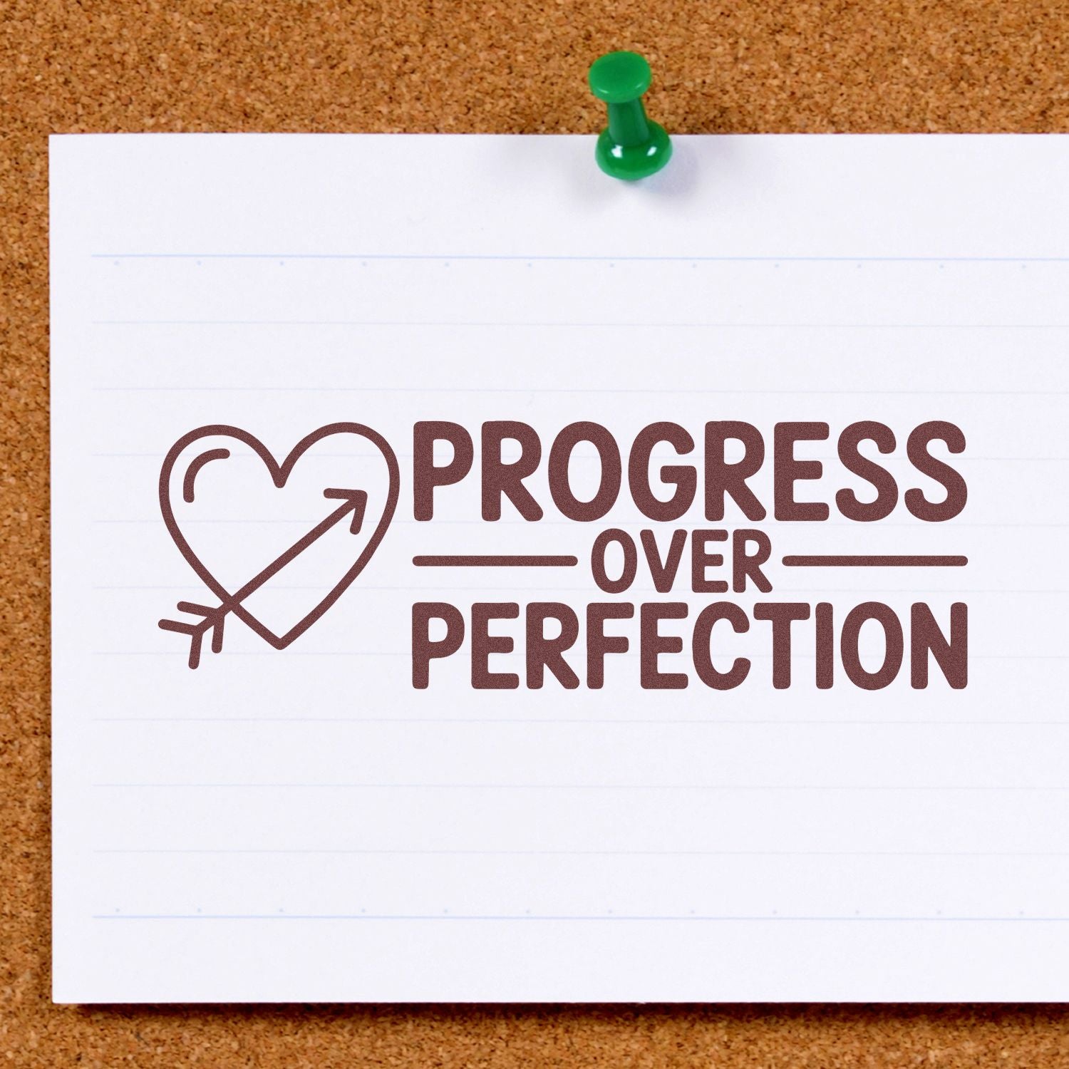 Brown stamp/seal reading Progress Over Perfection with heart-arrow, on white lined paper pinned by a green pushpin.