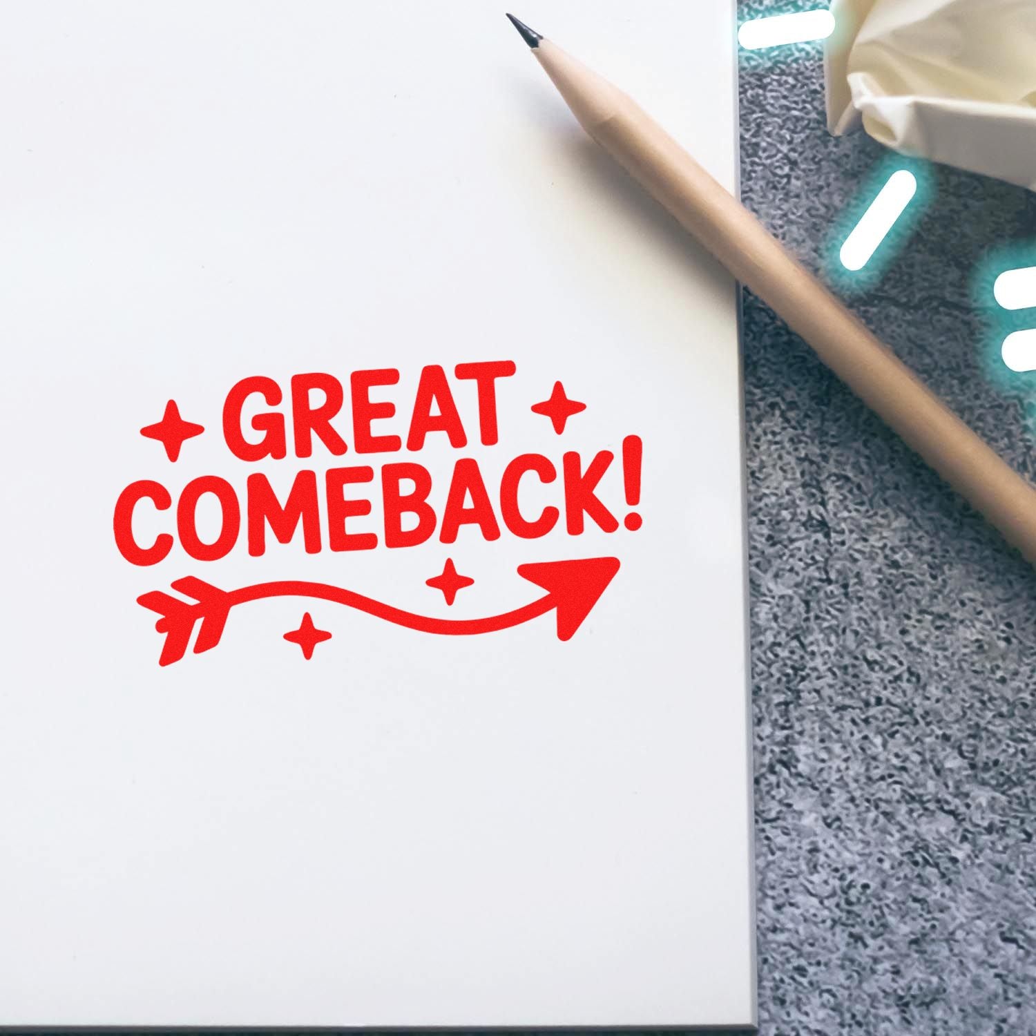 Red stamp and seal reading Great Comeback! with arrow on white notebook, beside a pencil on a gray textured surface.
