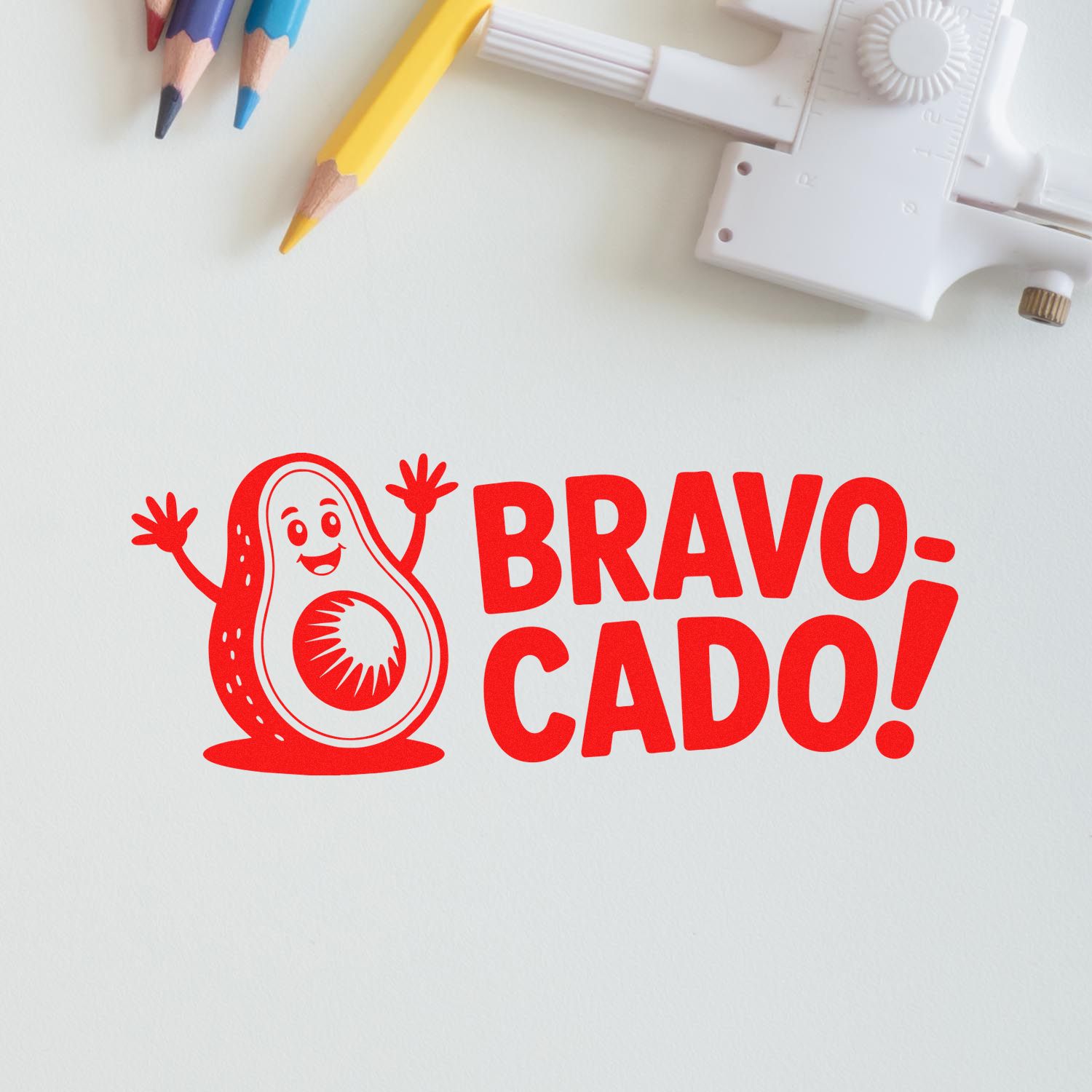Red BRAVO-CADO! avocado stamp design with white seal tool and yellow, blue, pink pencils on a white background
