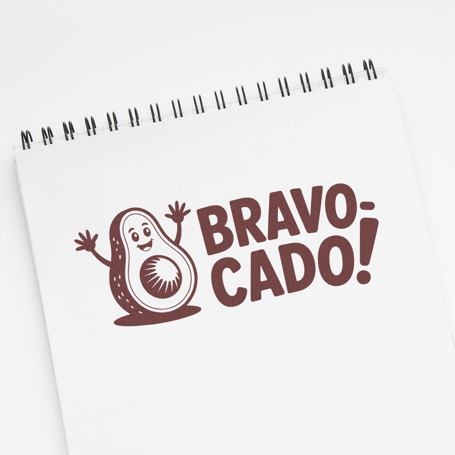 White spiral notebook with brown Bravo Cado! avocado stamp and seal design