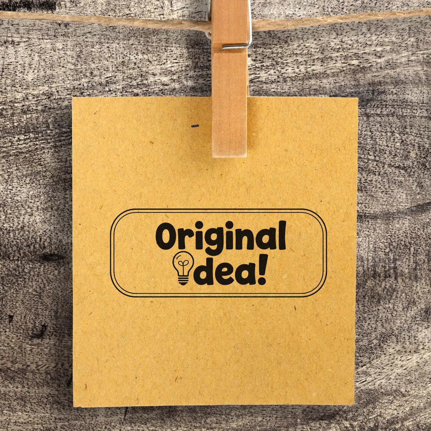 Kraft paper tag clipped to rustic wood with black Original idea! stamp and lightbulb seal.