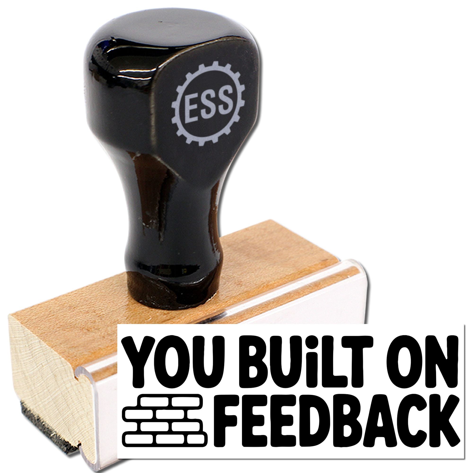Black custom stamp seal with ESS gear logo, mounted on a wooden block with white base and bold You Built on Feedback text.