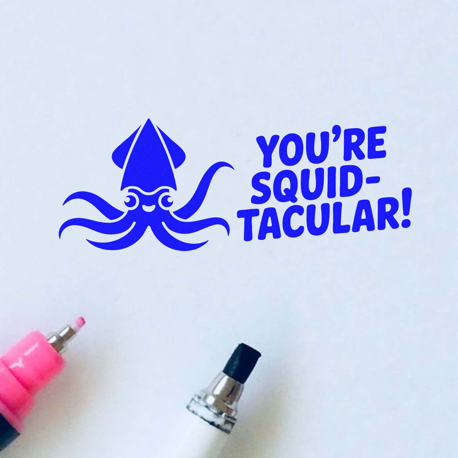 Blue squid stamp and seal design with Youre squid-tacular! text, plus pink and black stamping tools on white paper.