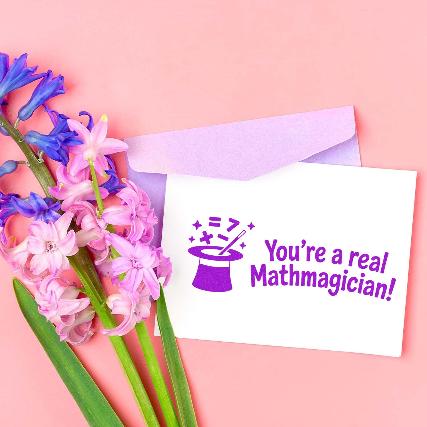Purple custom stamp and seal on white card saying Youre a real Mathmagician! with lilac envelope and pink-blue flowers.