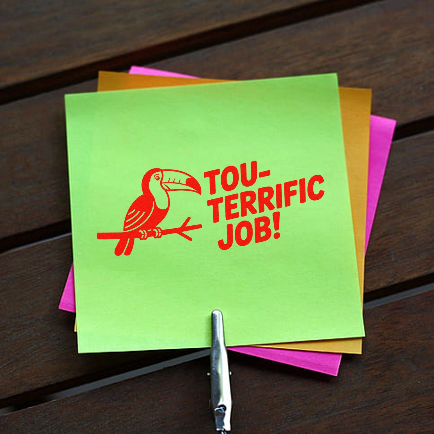 Neon green card stamped with red toucan Tou-terrific Job! rubber seal, layered over pink and orange notes.
