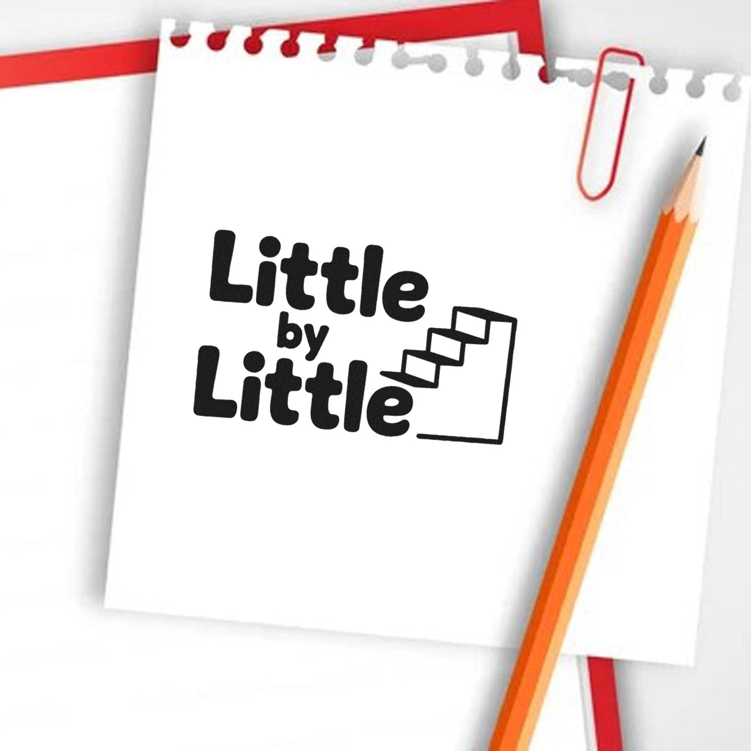 Black Little by Little stamp and seal logo on white notepad, with red paperclip and orange pencil