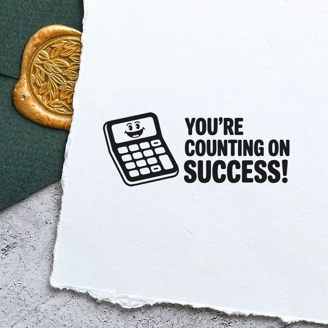 Black rubber success stamp with smiling calculator on white paper beside a gold embossed seal, on dark green.