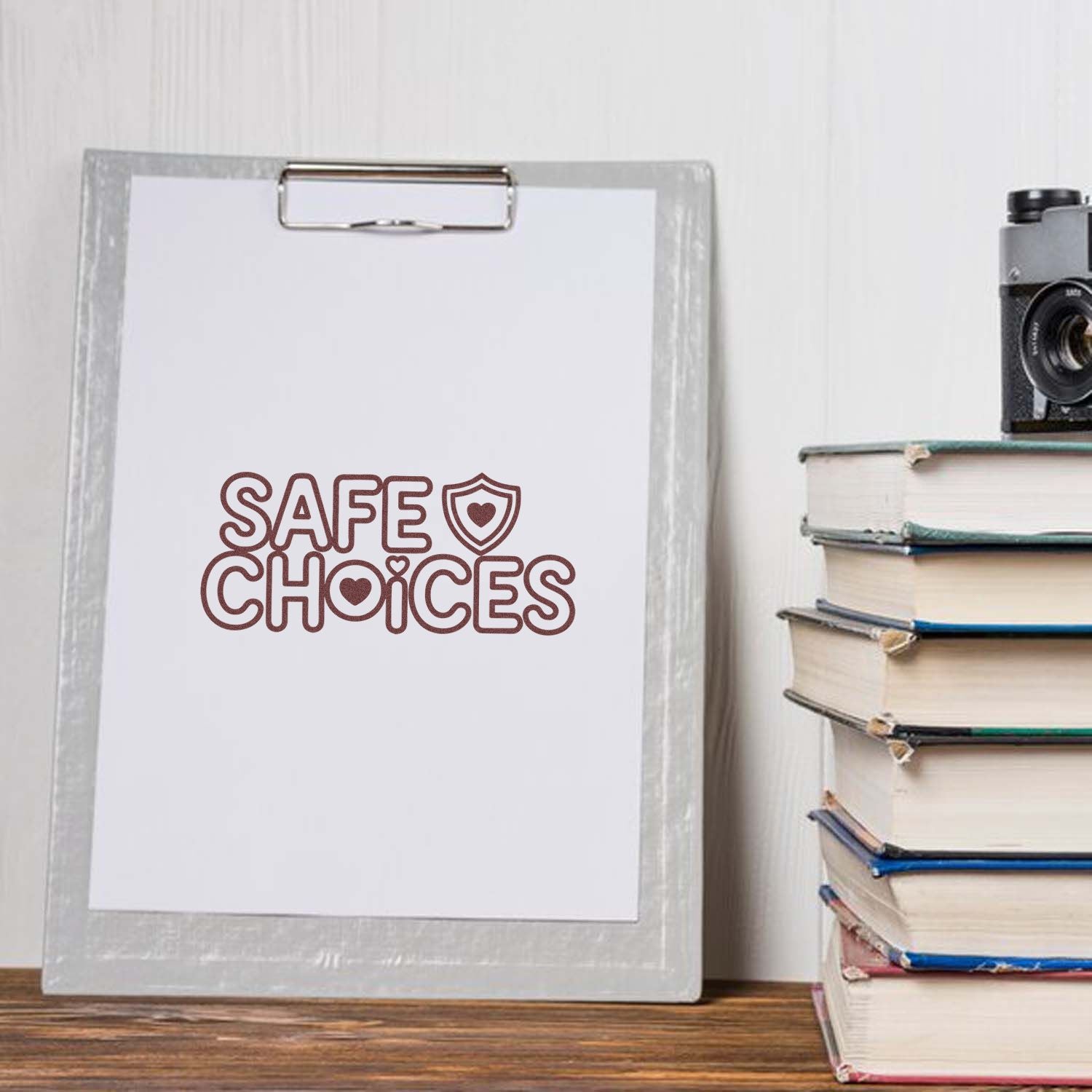 Maroon Safe Choices stamp seal on a white clipboard beside stacked books and a vintage camera
