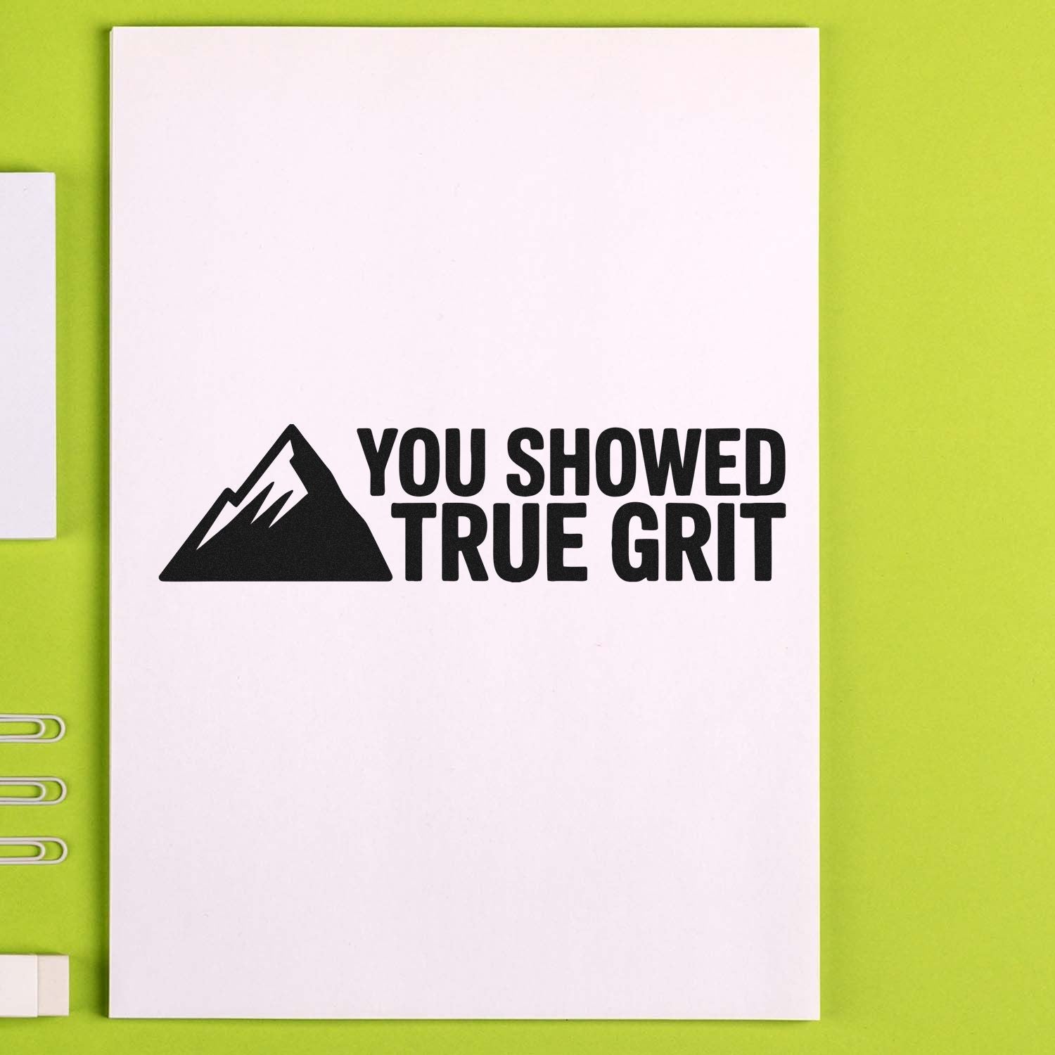 Custom stamp and seal with black mountain logo and You Showed True Grit on white paper, against lime green background.