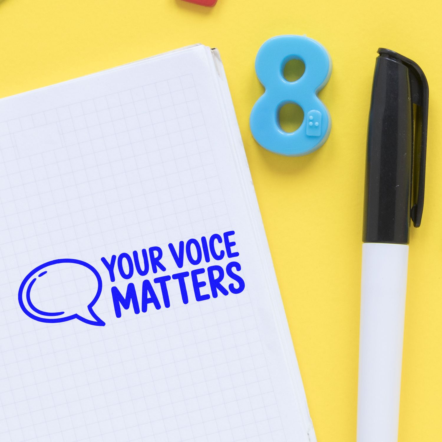 Blue Your Voice Matters stamp and speech bubble seal on a notebook page, with black marker on a yellow background