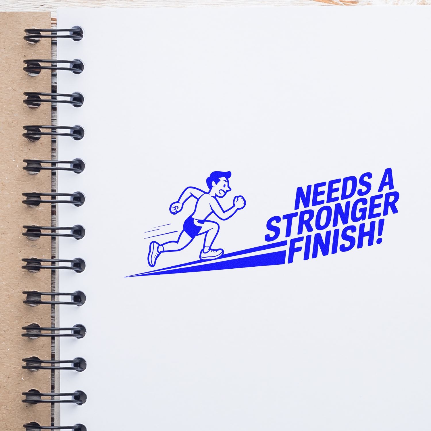 Blue custom stamp seal on white spiral notebook: running figure and bold blue text, NEEDS A STRONGER FINISH!