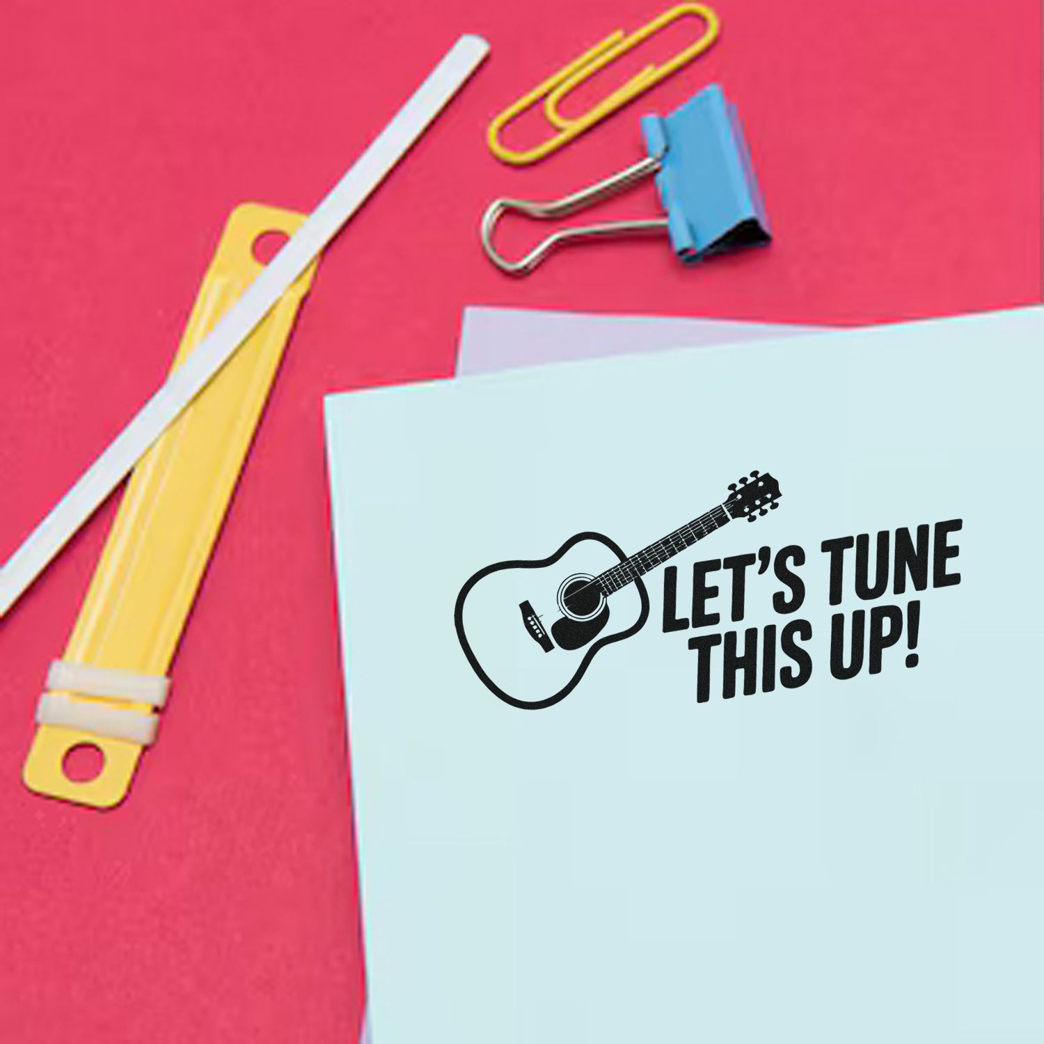 Custom stamp and seal design: black guitar logo and Lets Tune This Up! on light blue paper, pink background with clips.