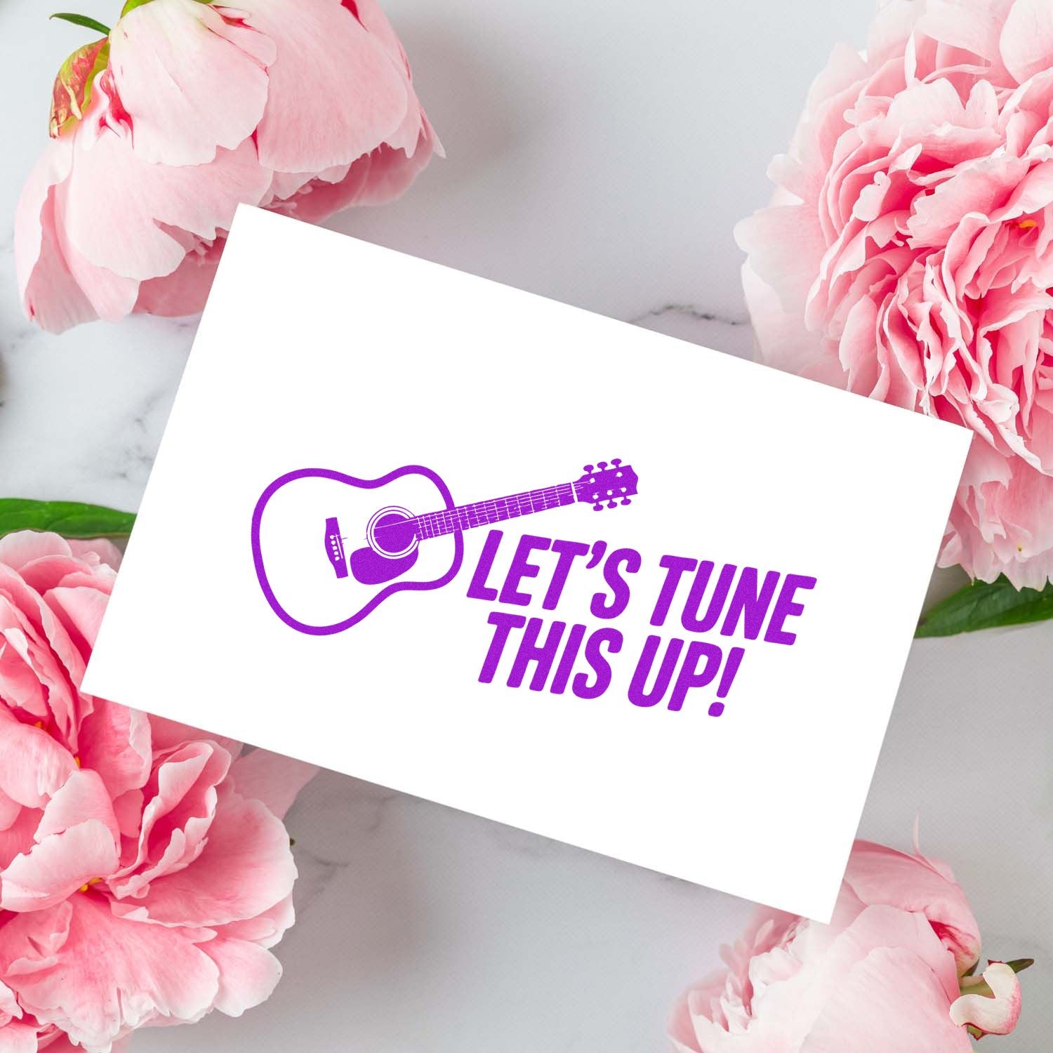 Purple guitar stamp with LETS TUNE THIS UP! on a white card, surrounded by pink peonies.