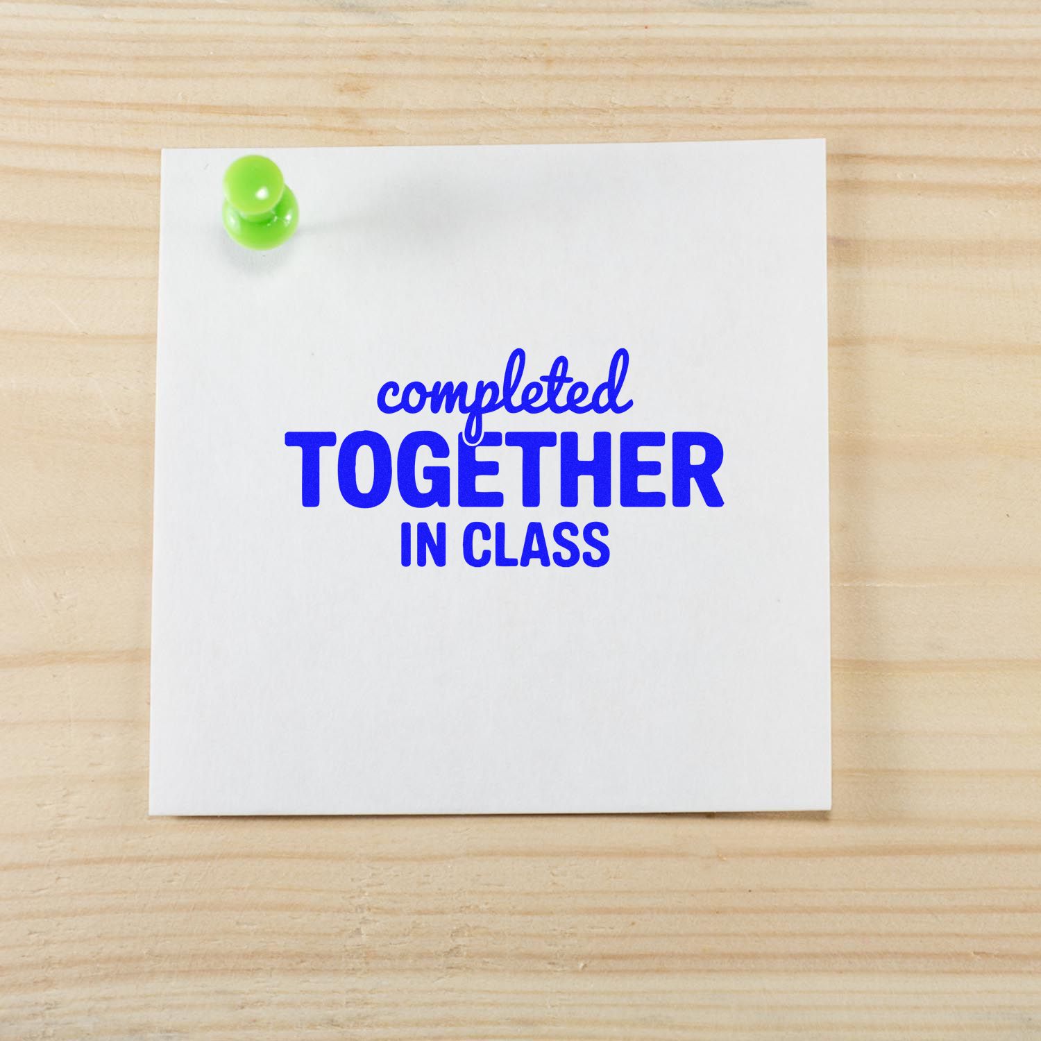 Blue classroom stamp reading completed together in class on white paper, pinned with a lime green pushpin.