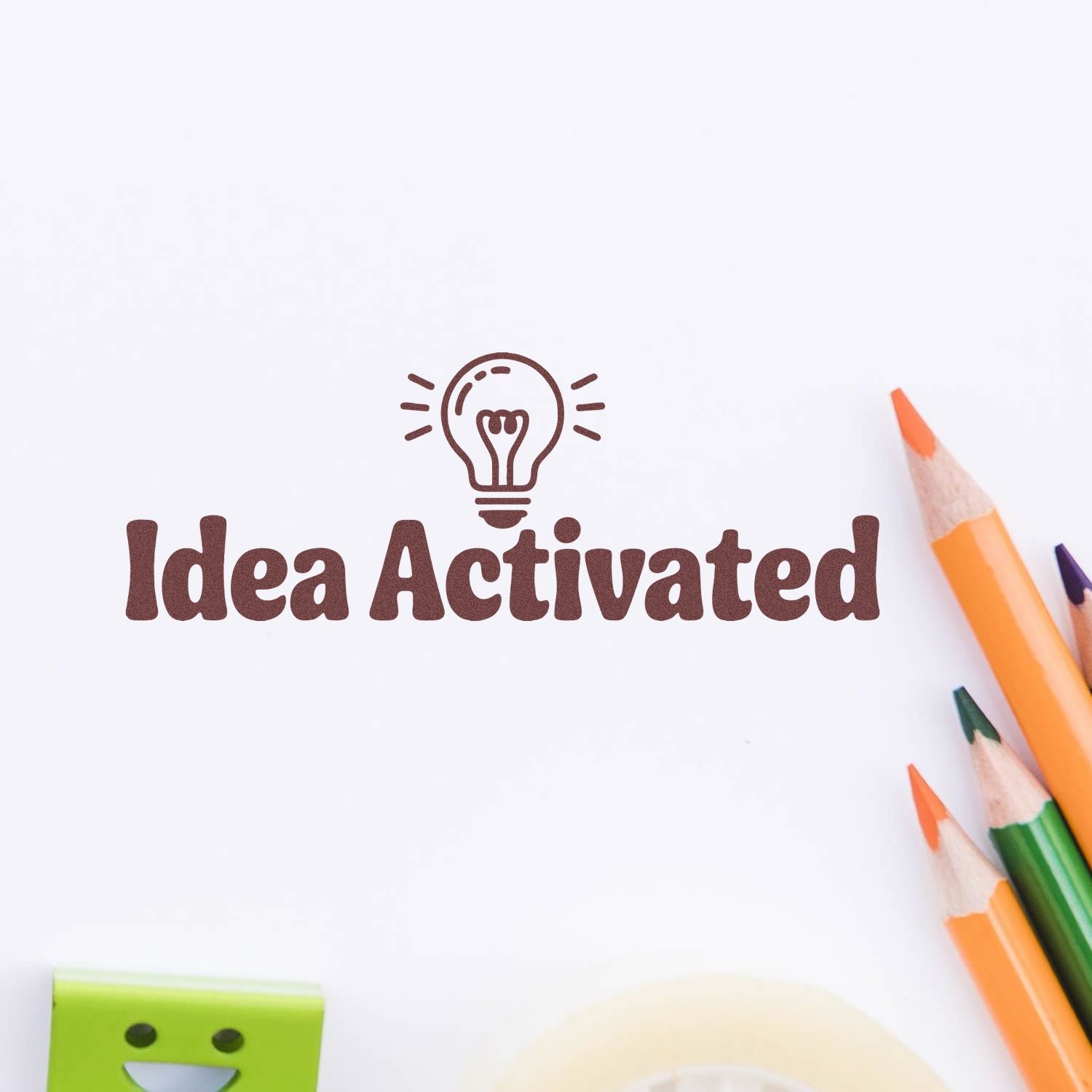 Brown Idea Activated stamp seal with lightbulb icon on white paper, beside orange and green pencils.