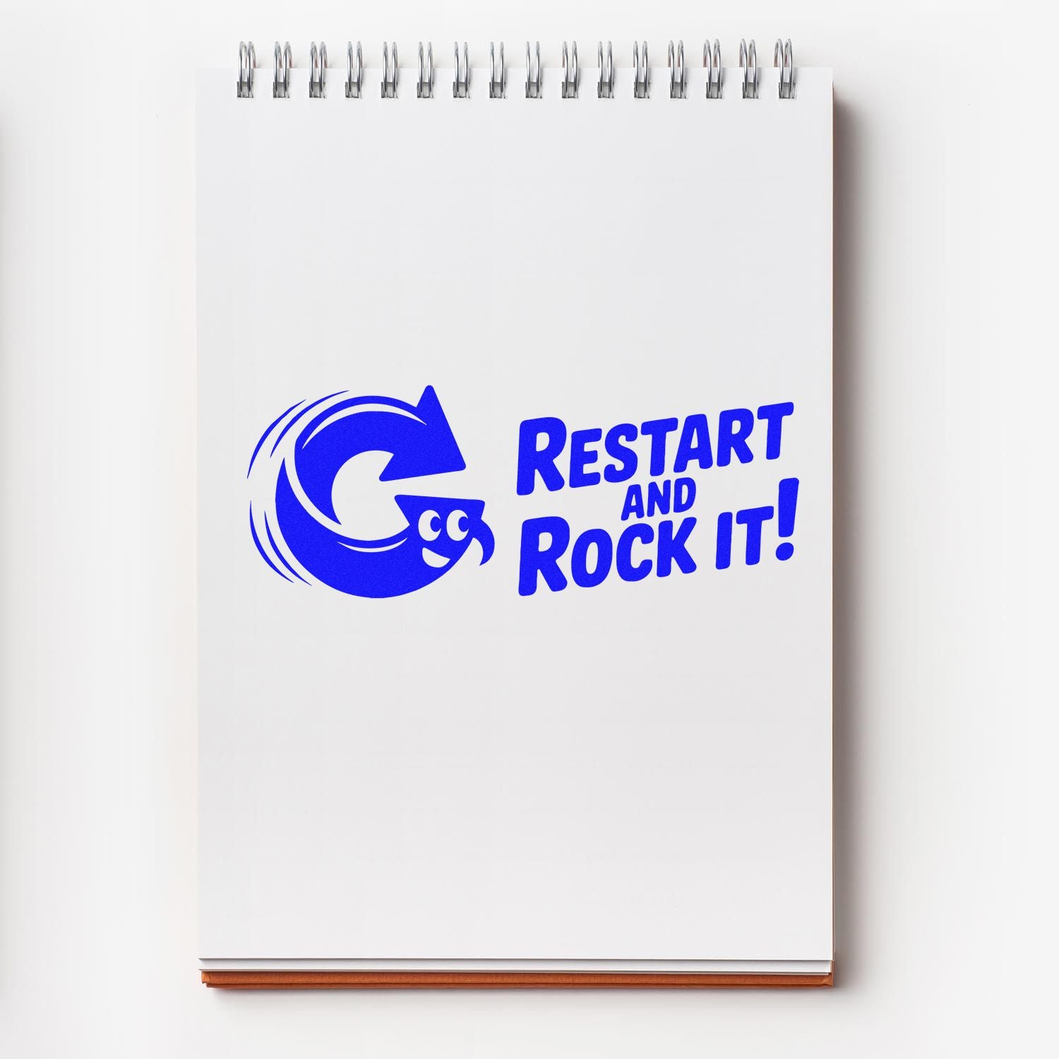 Blue stamp seal on white spiral notepad with circular arrow logo and Restart and Rock It! text.