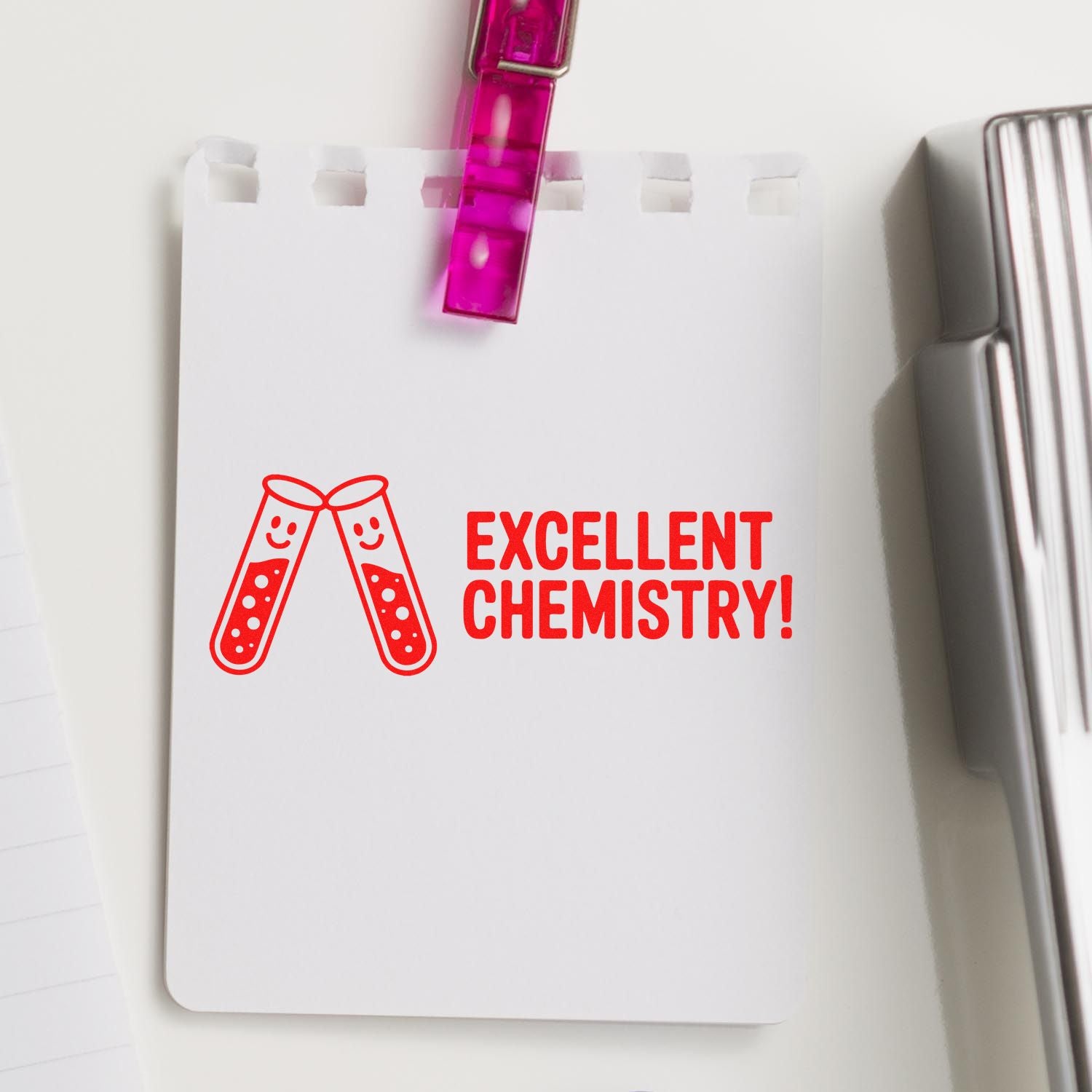 Red Excellent Chemistry! stamp with test tubes on white paper, clipped by a pink clip.