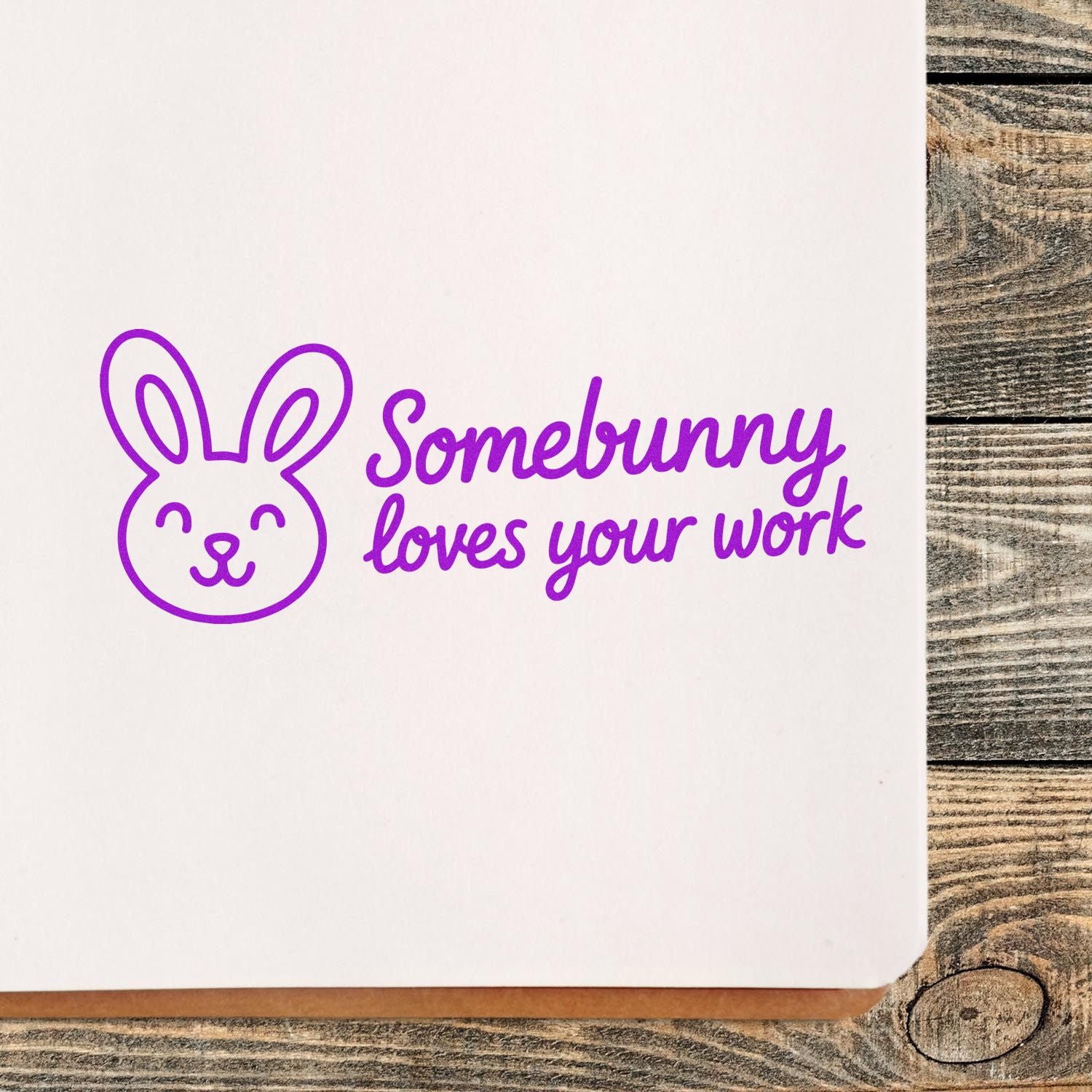Purple bunny stamp/seal with Somebunny loves your work in purple on white paper over rustic wood.