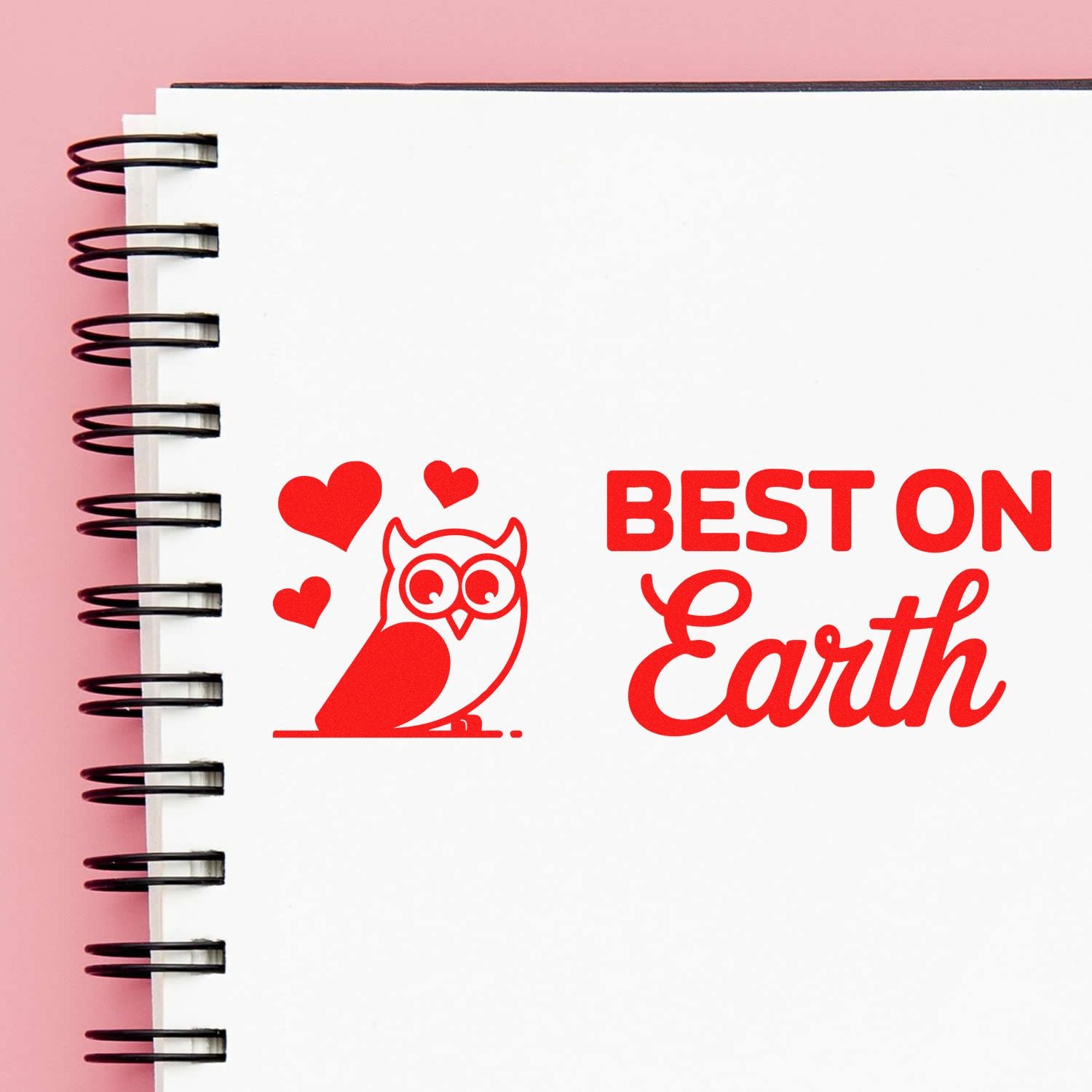 Red stamp and seal design with owl, hearts, and BEST ON Earth on a white spiral notebook against a pink background.