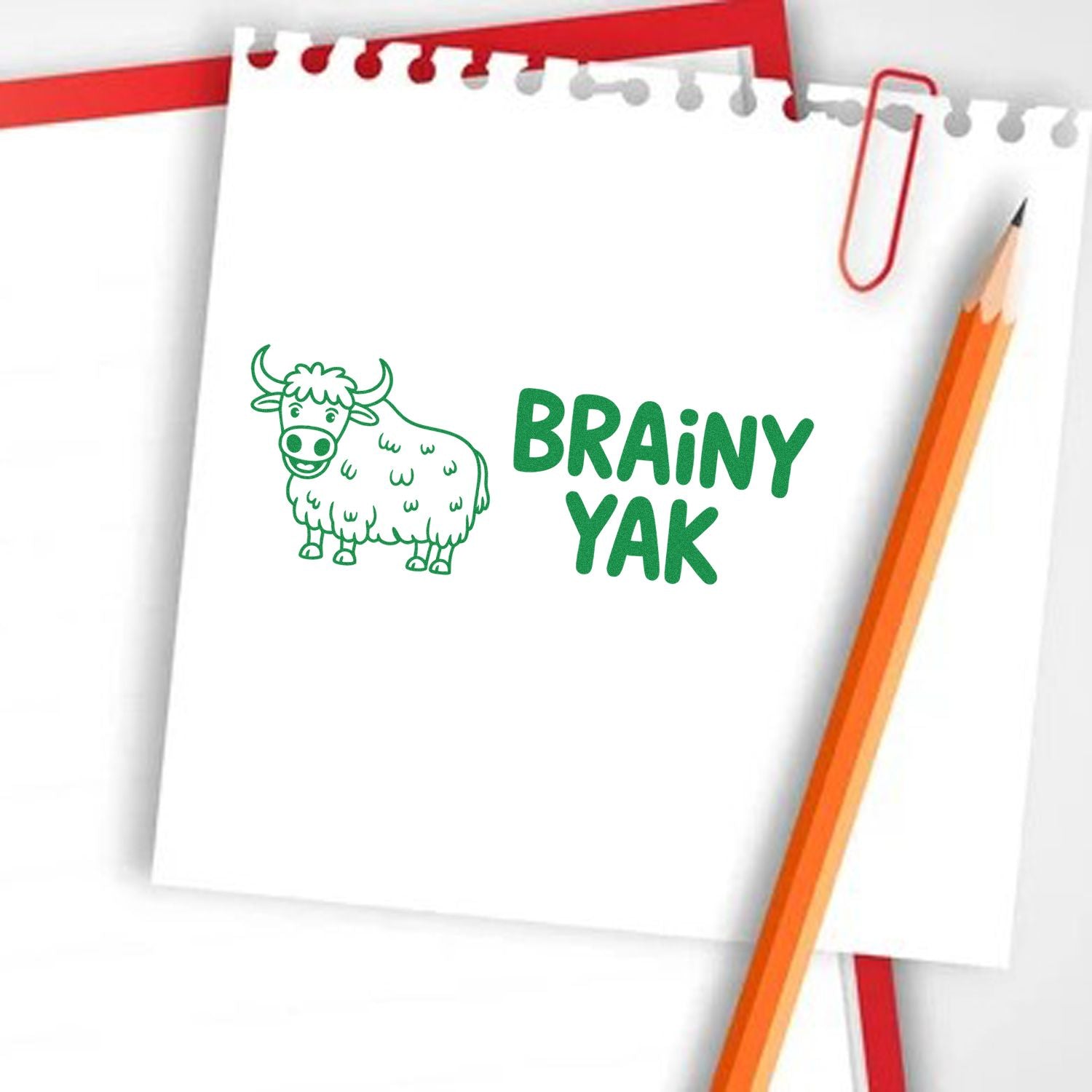 Green Brainy Yak stamp and seal on white notepad, with cartoon yak, orange pencil, and red paperclip.