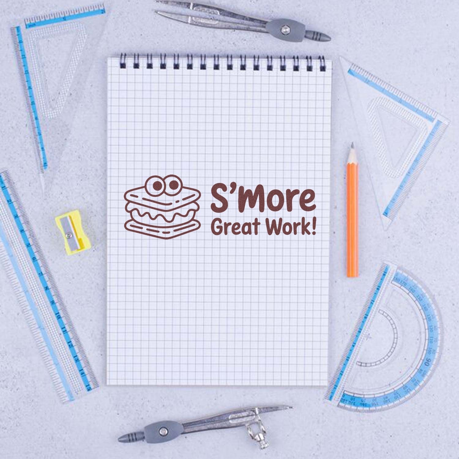 Brown S'more Great Work! stamp seal with cartoon s'more on graph paper, framed by blue drafting tools.