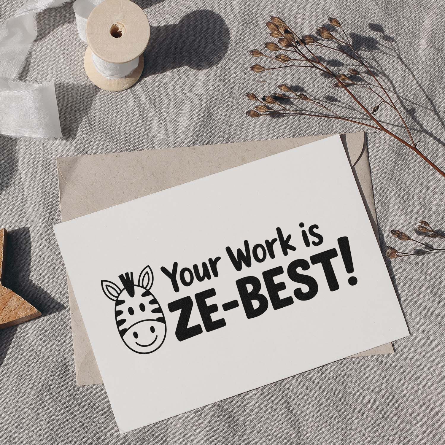 Custom black zebra stamp and seal reading Your Work is ZE-BEST! on white card, beige envelope, ribbon spool, dried stems.