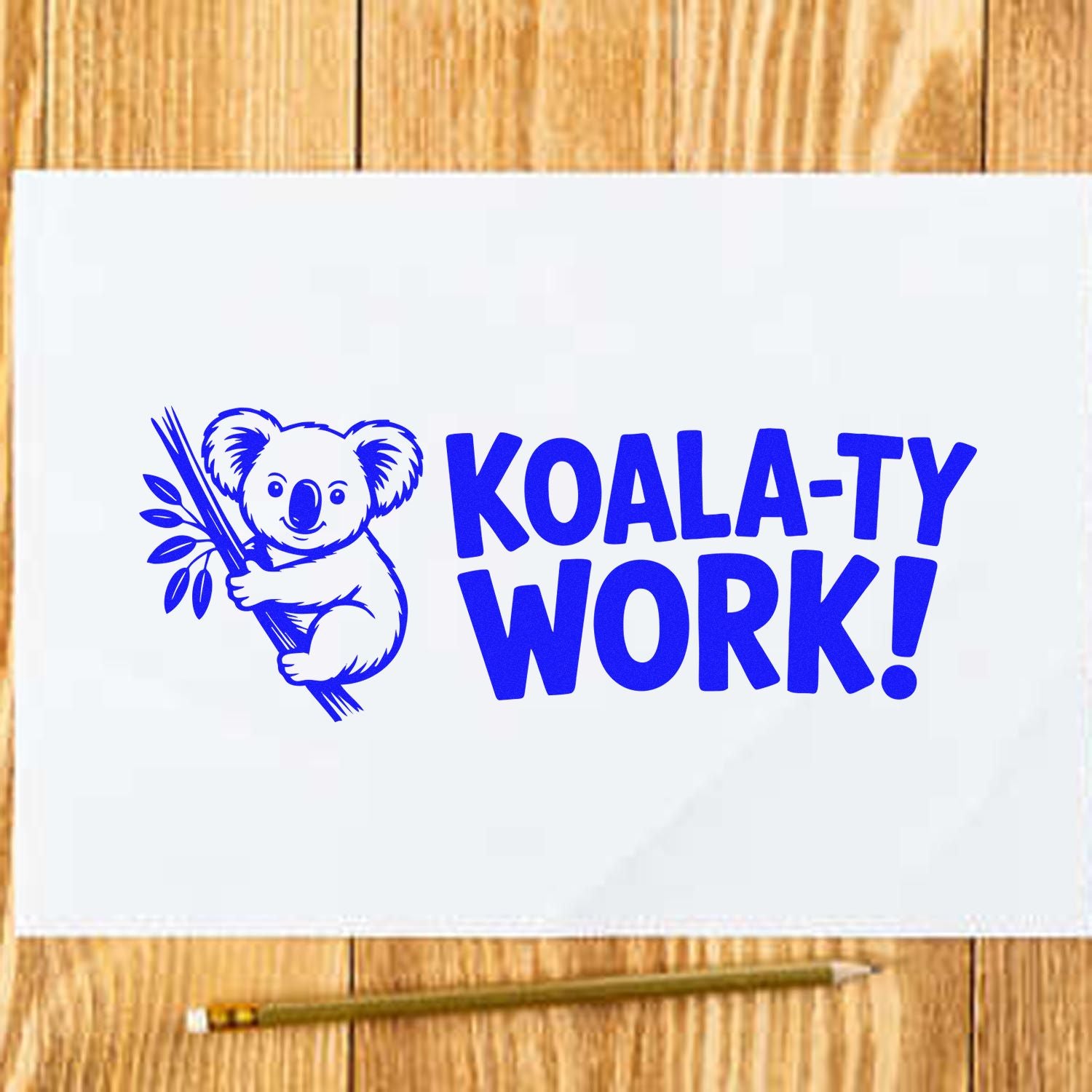 Blue KOALA-TY WORK stamp seal with a koala holding a branch on white paper over a wood background.
