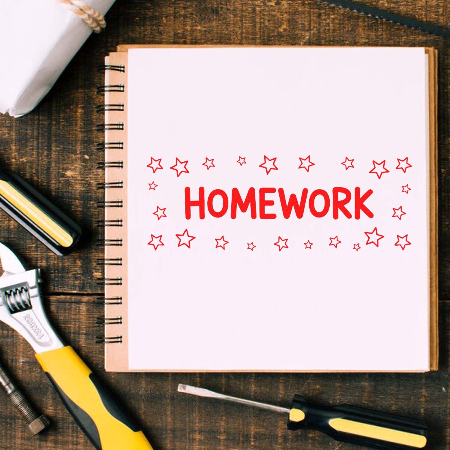 Red homework stamp and star seal on a spiral notebook, with tools on a rustic wooden desk.