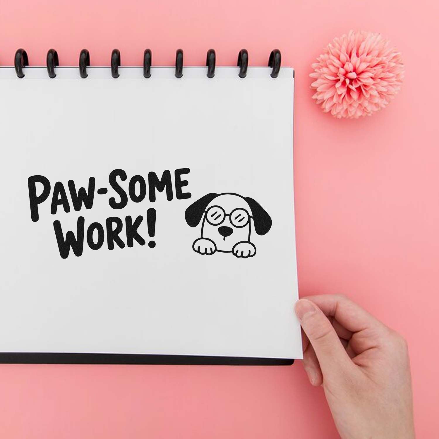 Paw-some Work! dog stamp and seal on white spiral notebook, pink background, with flower accent.