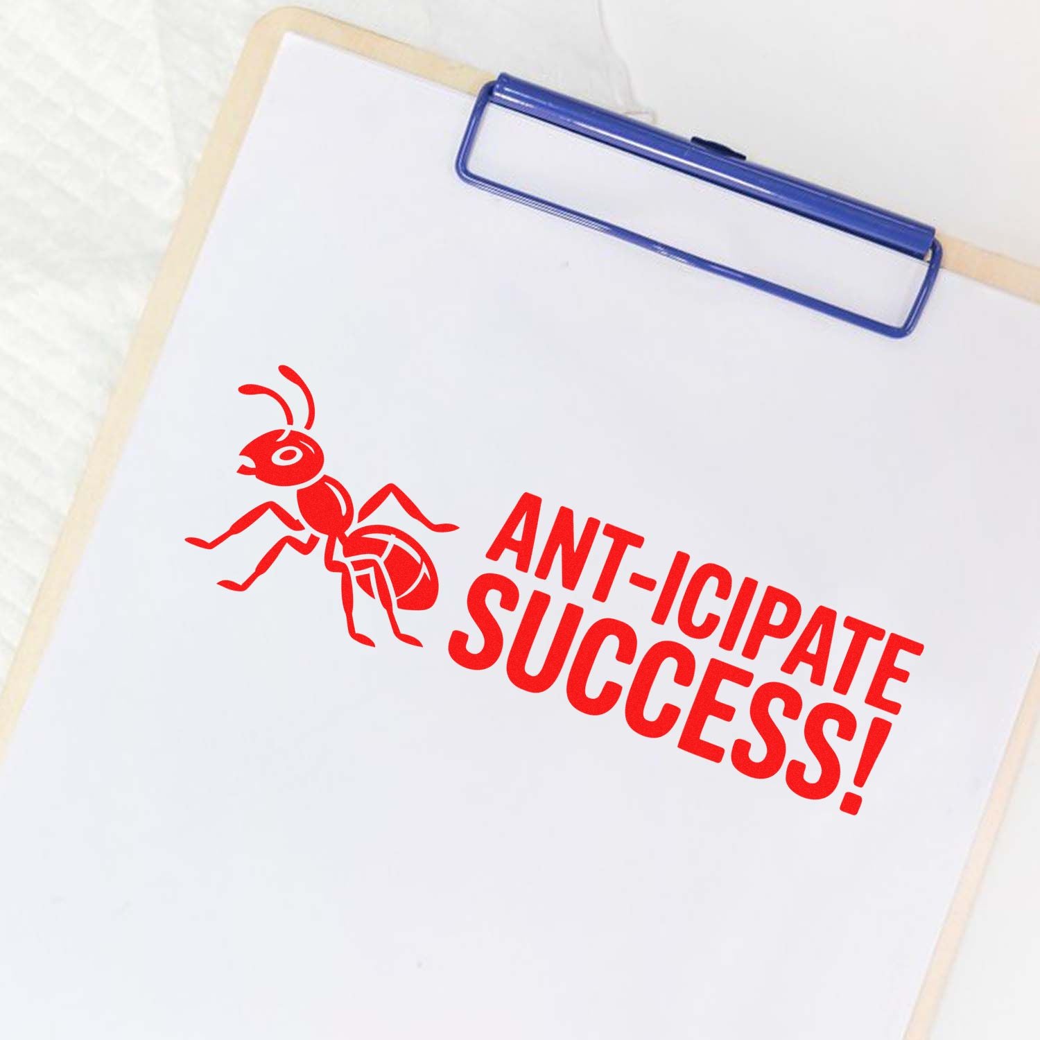 Blue clipboard with a red ant stamp and seal reading ANT-ICIPATE SUCCESS! on white paper.