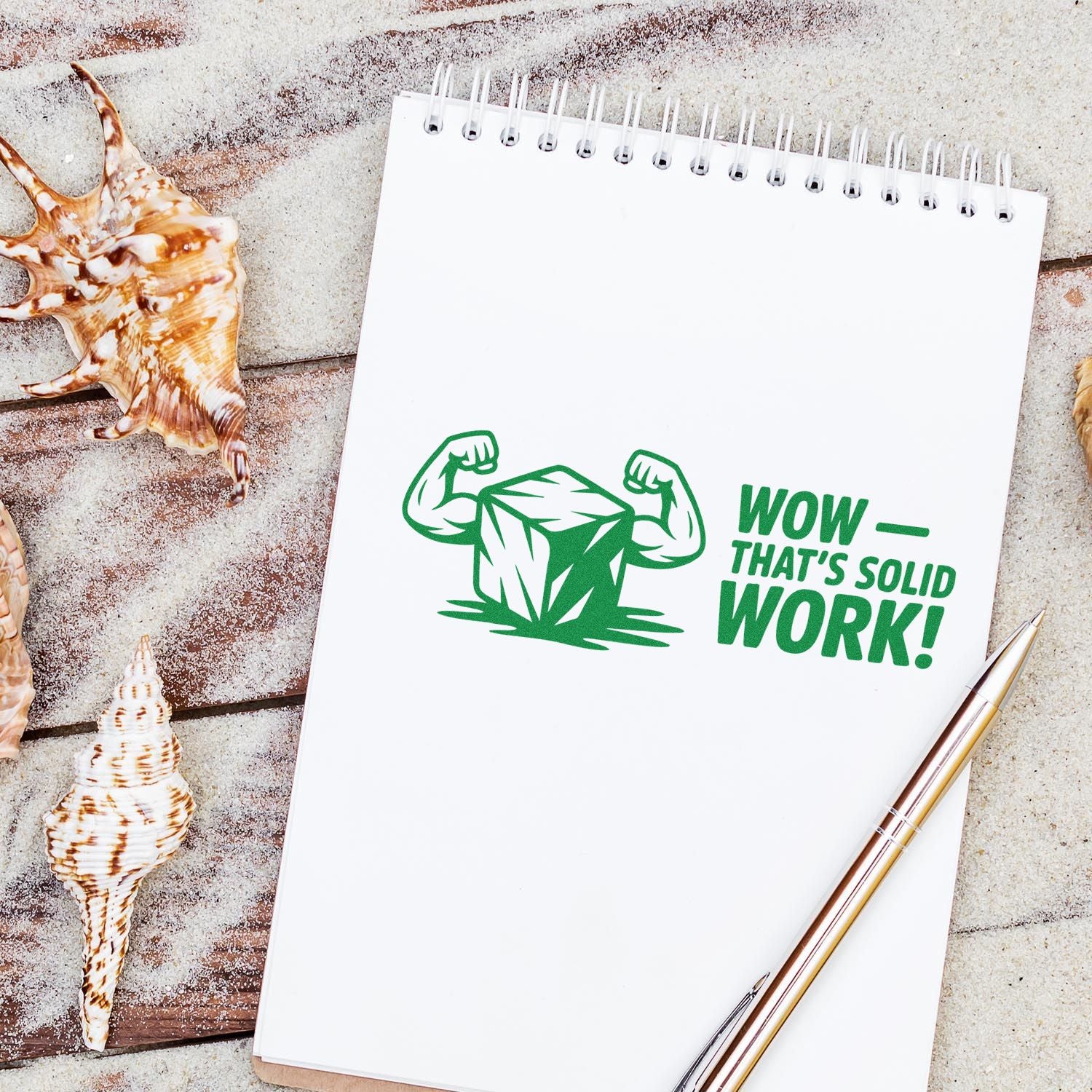 Green custom stamp seal on white spiral notebook, featuring a flexing ice cube and Wowthats solid work! beside seashells.