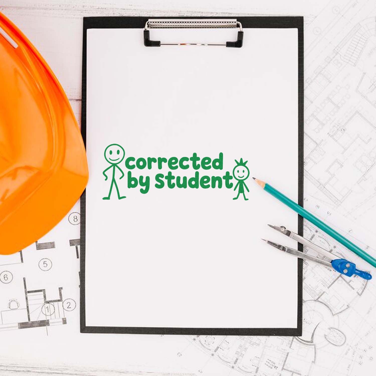 Green corrected by student correction stamp on clipboard with orange hard hat, pencils, and architectural plans