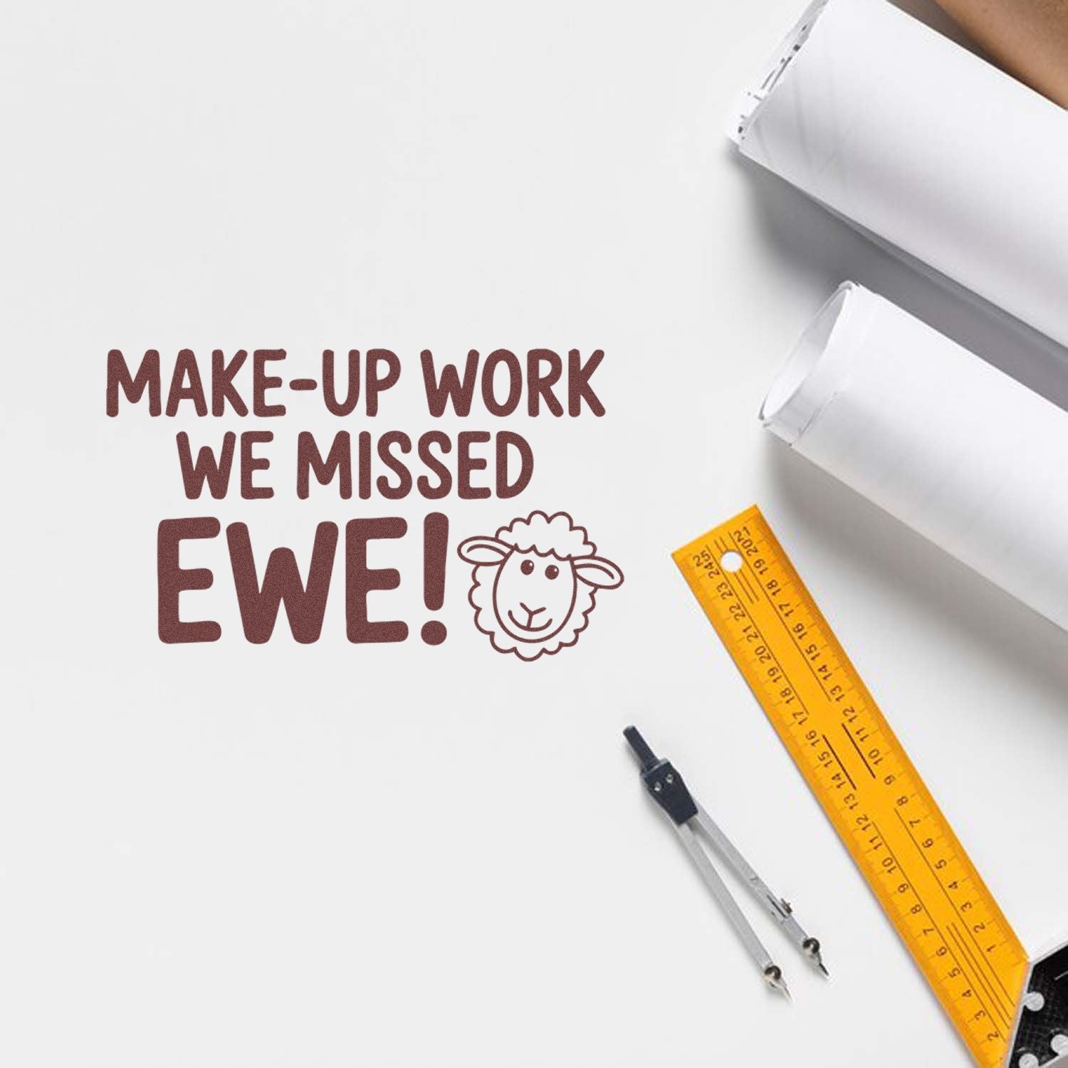 Maroon stamp and seal reading MAKE-UP WORK WE MISSED EWE! with sheep icon, beside white paper, yellow ruler, and compass.