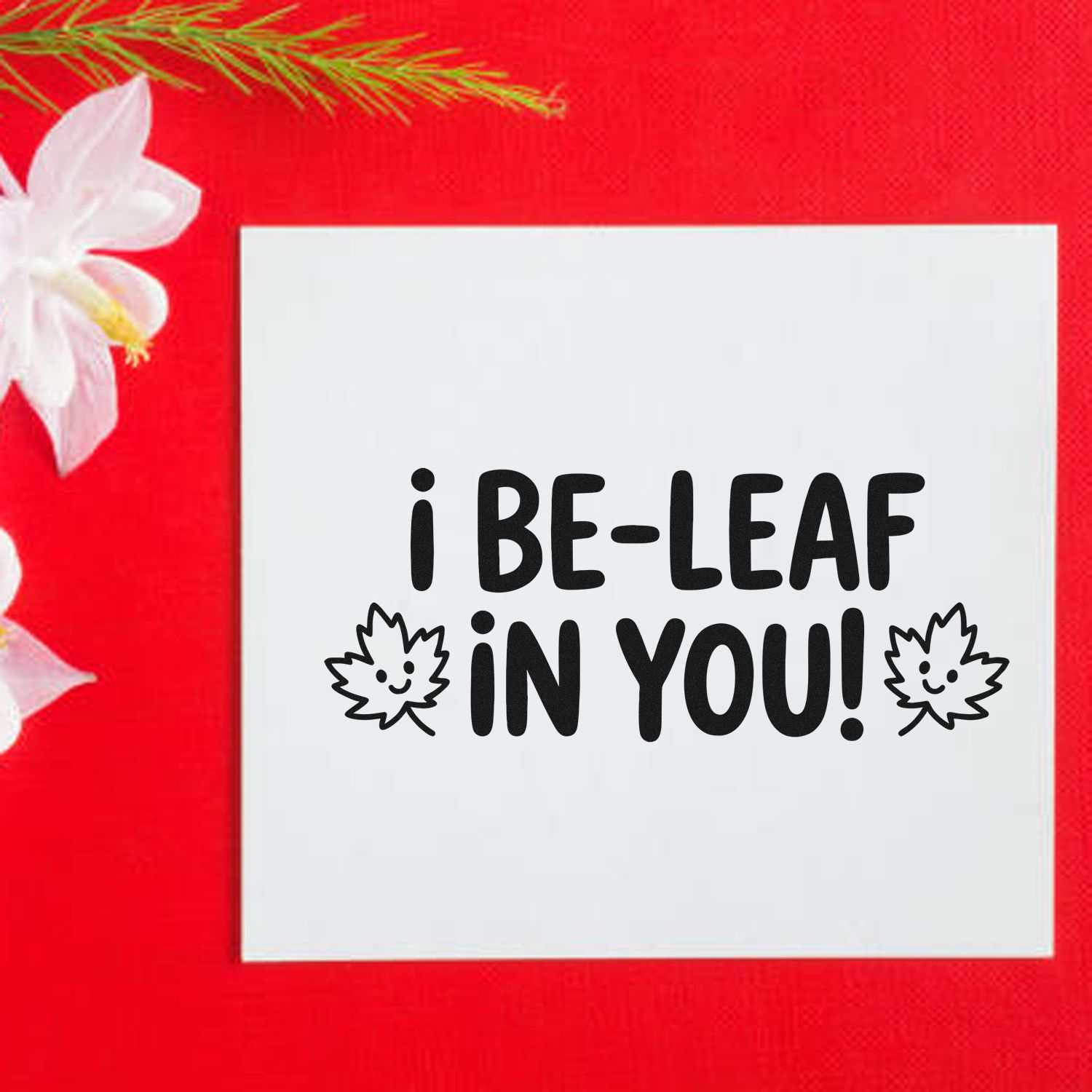 White stamp and seal with black i BE-LEAF IN YOU! text and leaf icons on a bright red background.