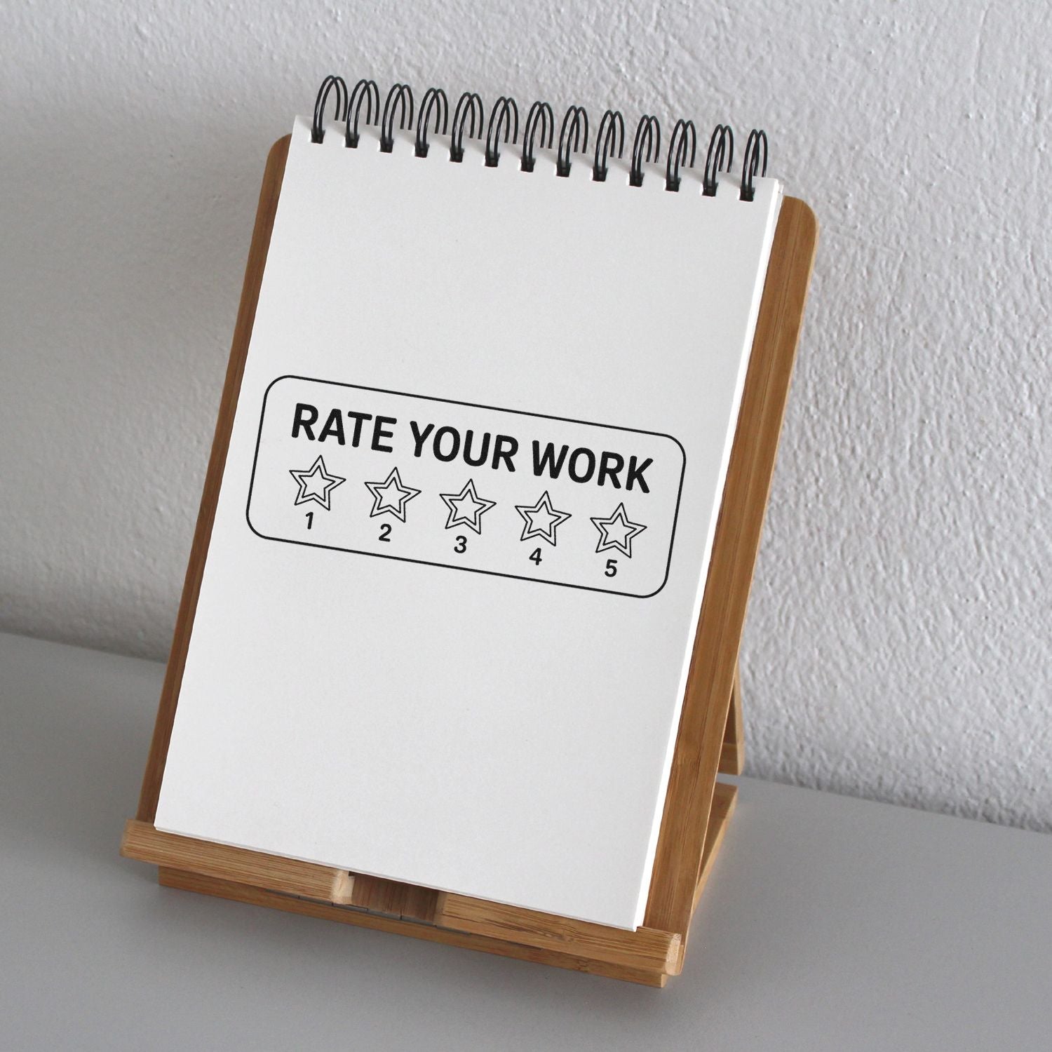 White spiral notepad on wooden stand showing a black Rate Your Work five-star stamp and seal design.