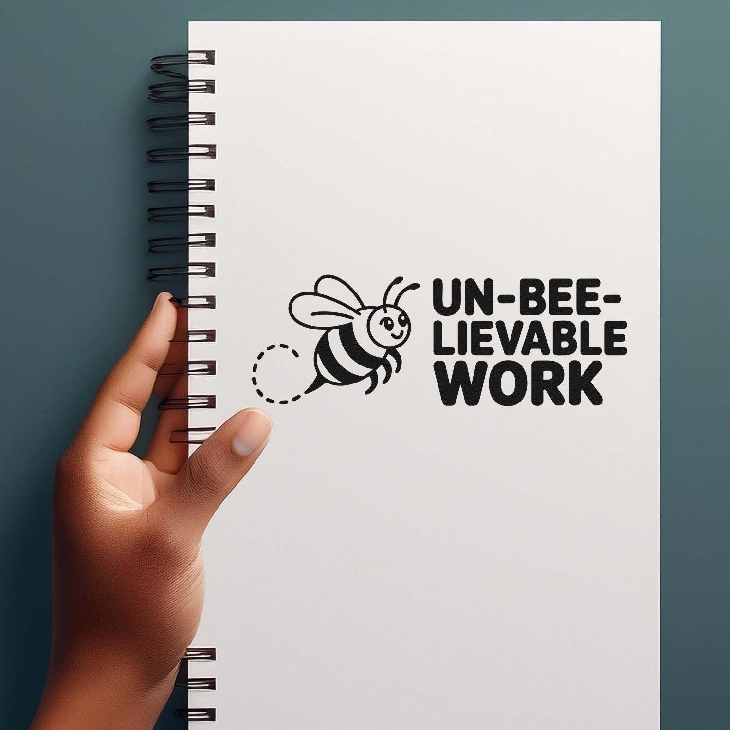 Black bee stamp and seal design on white spiral notebook cover reading UN-BEE-LIEVABLE WORK against teal background.