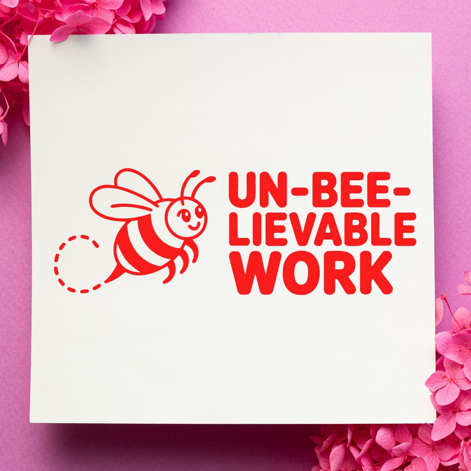 Red bee stamp seal reading UN-BEE-LIEVABLE WORK on a white card, framed by pink flowers.