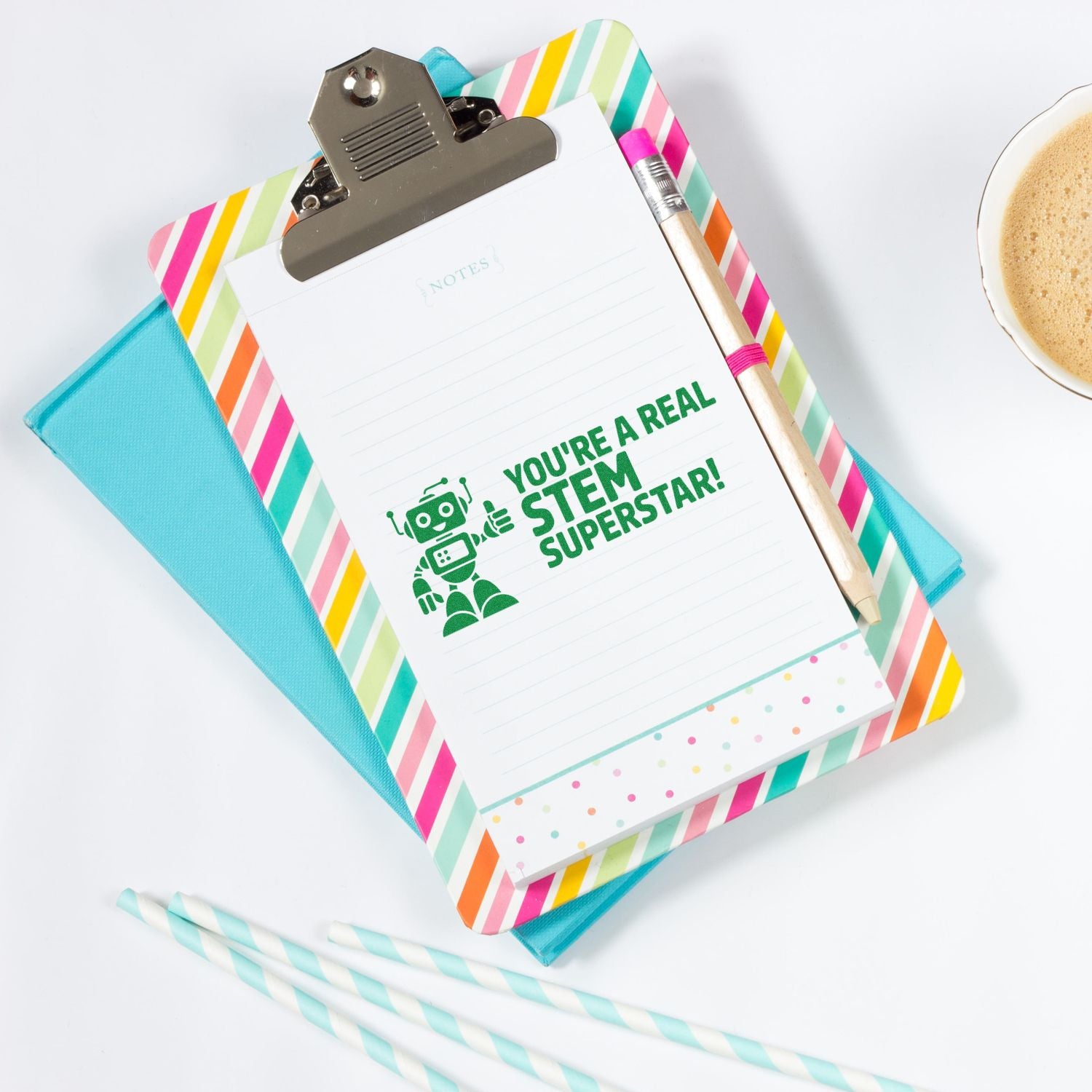 Pastel clipboard notepad with green STEM Superstar stamp, striped border, turquoise notebook, pencil, and coffee cup.